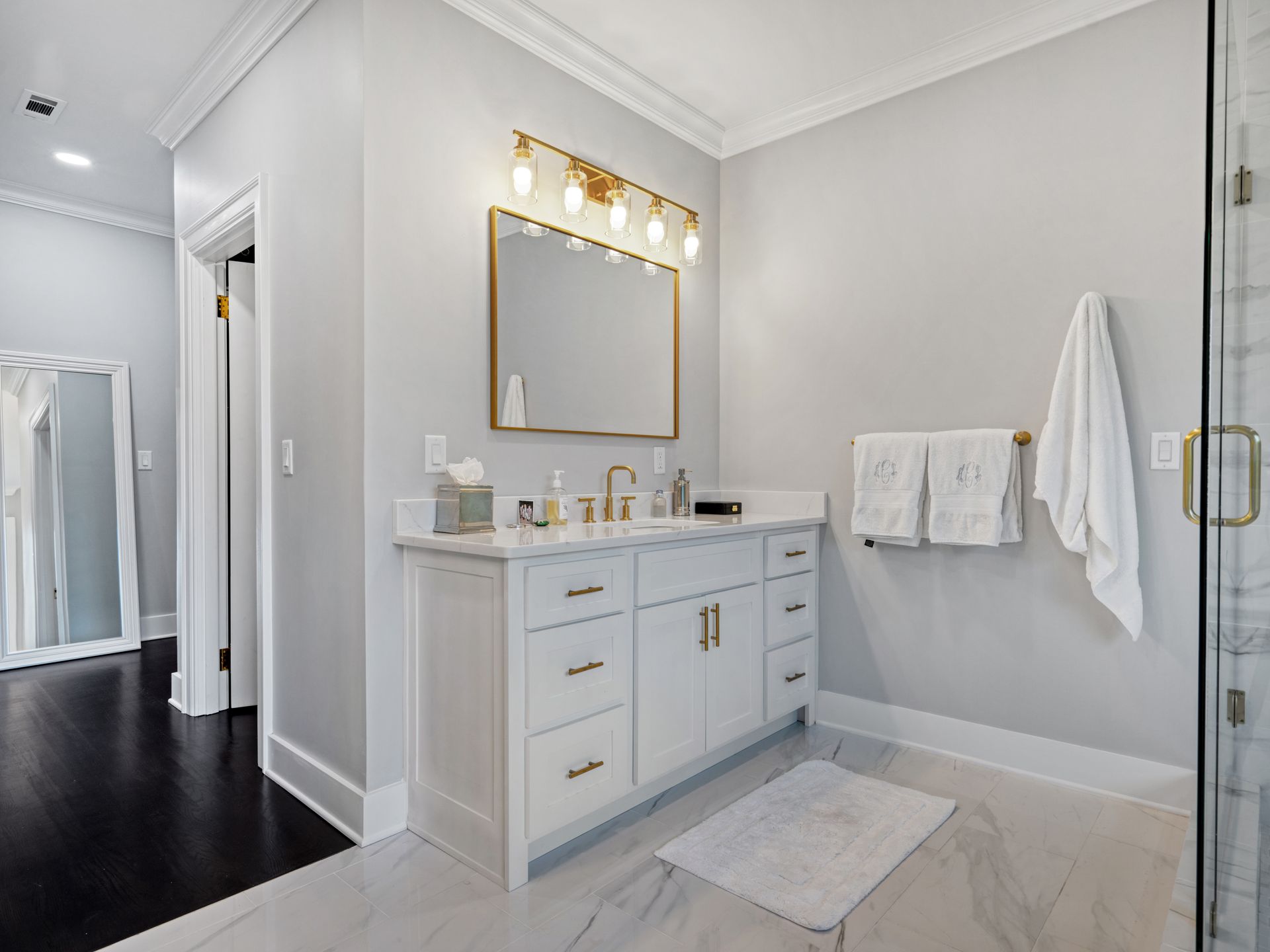 Elegant white bathroom with marble counters, gold fixtures, and a vanity.