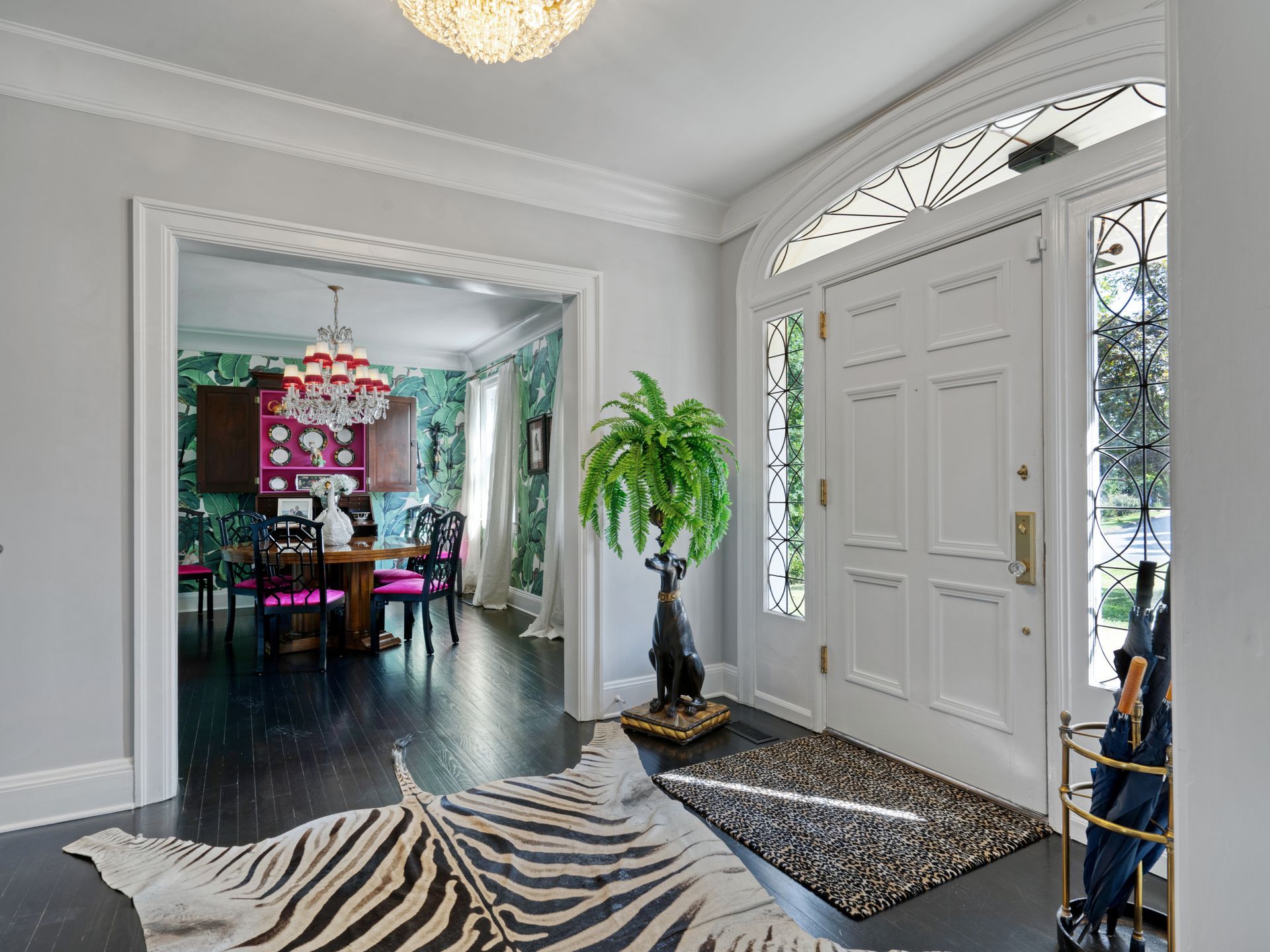 Entryway with white door, zebra rug, and view into dining room with green wallpaper and pink chairs.