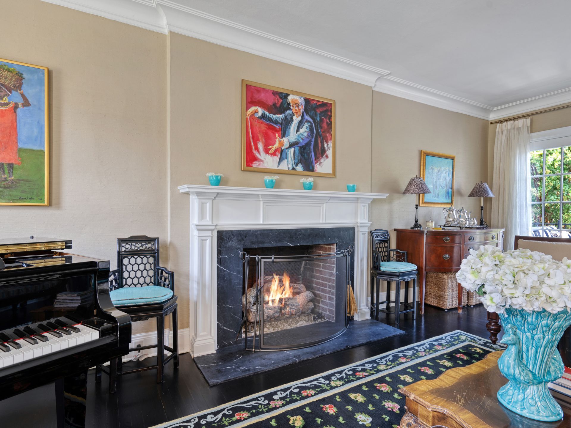 Living room with fireplace, piano, and art on beige walls. Fire burning in the fireplace.