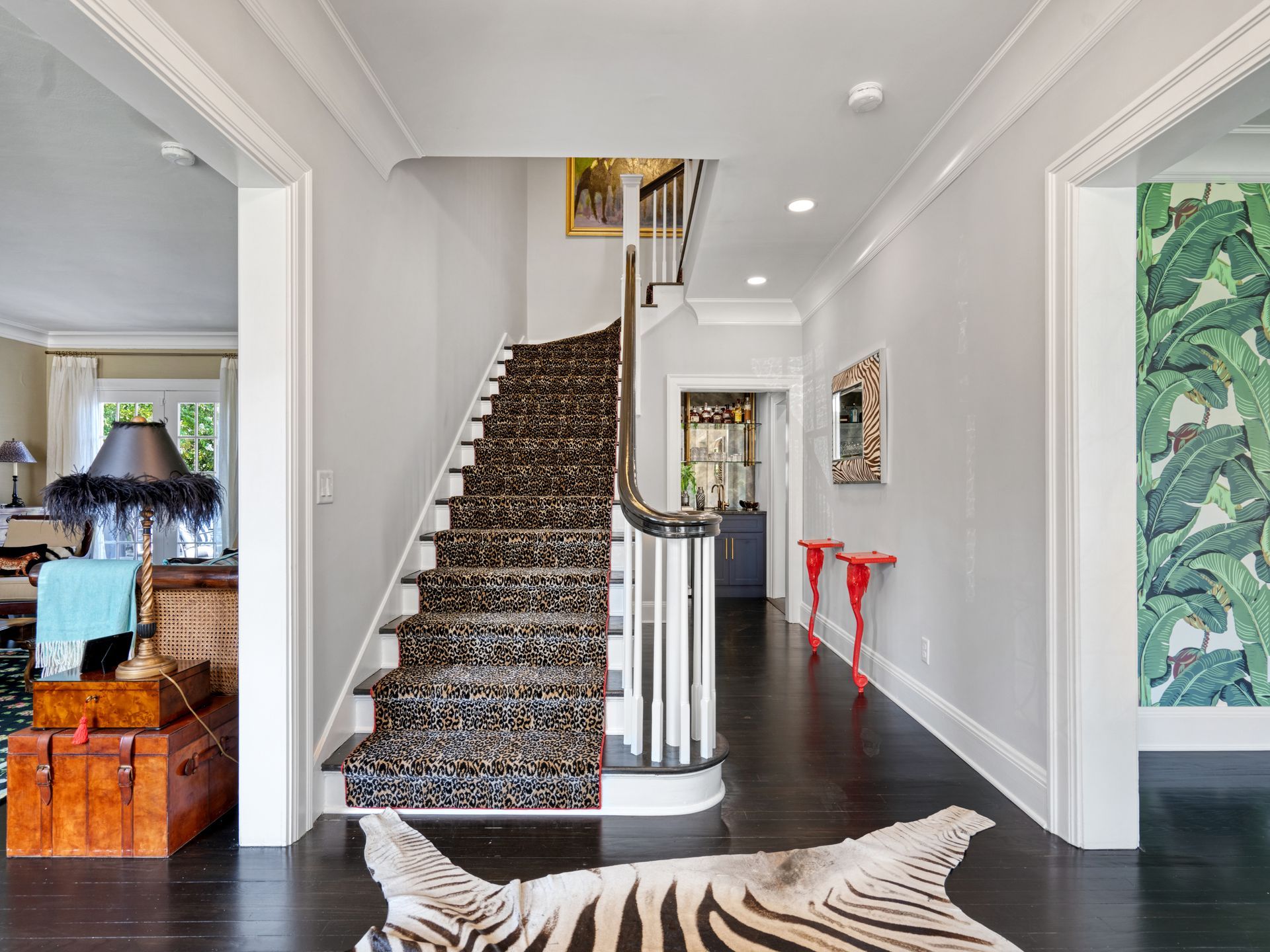 Entry hall with zebra rug, patterned stairs, and white walls, with a hallway to the right with patterned green wallpaper.
