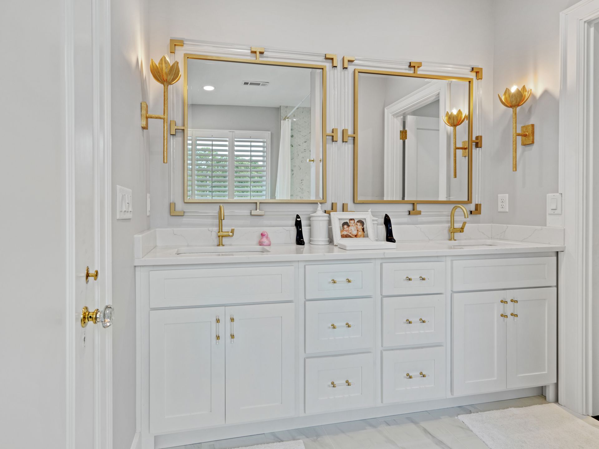 White bathroom vanity with two mirrors, gold accents, and matching sconces.