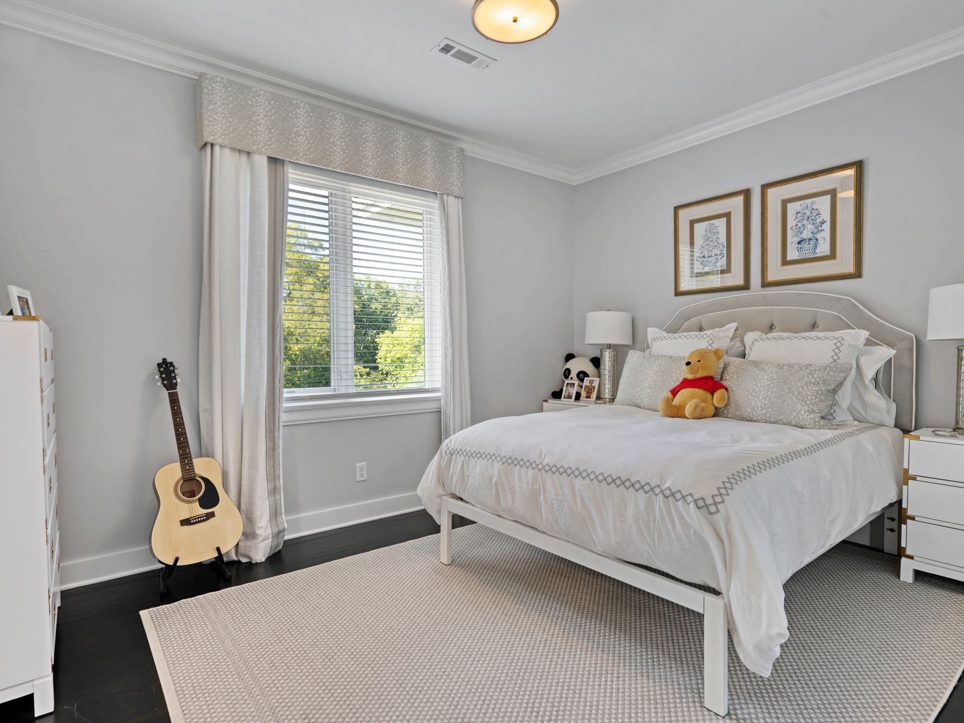 Bedroom with white bed, gray walls, guitar, and window with light streaming in.