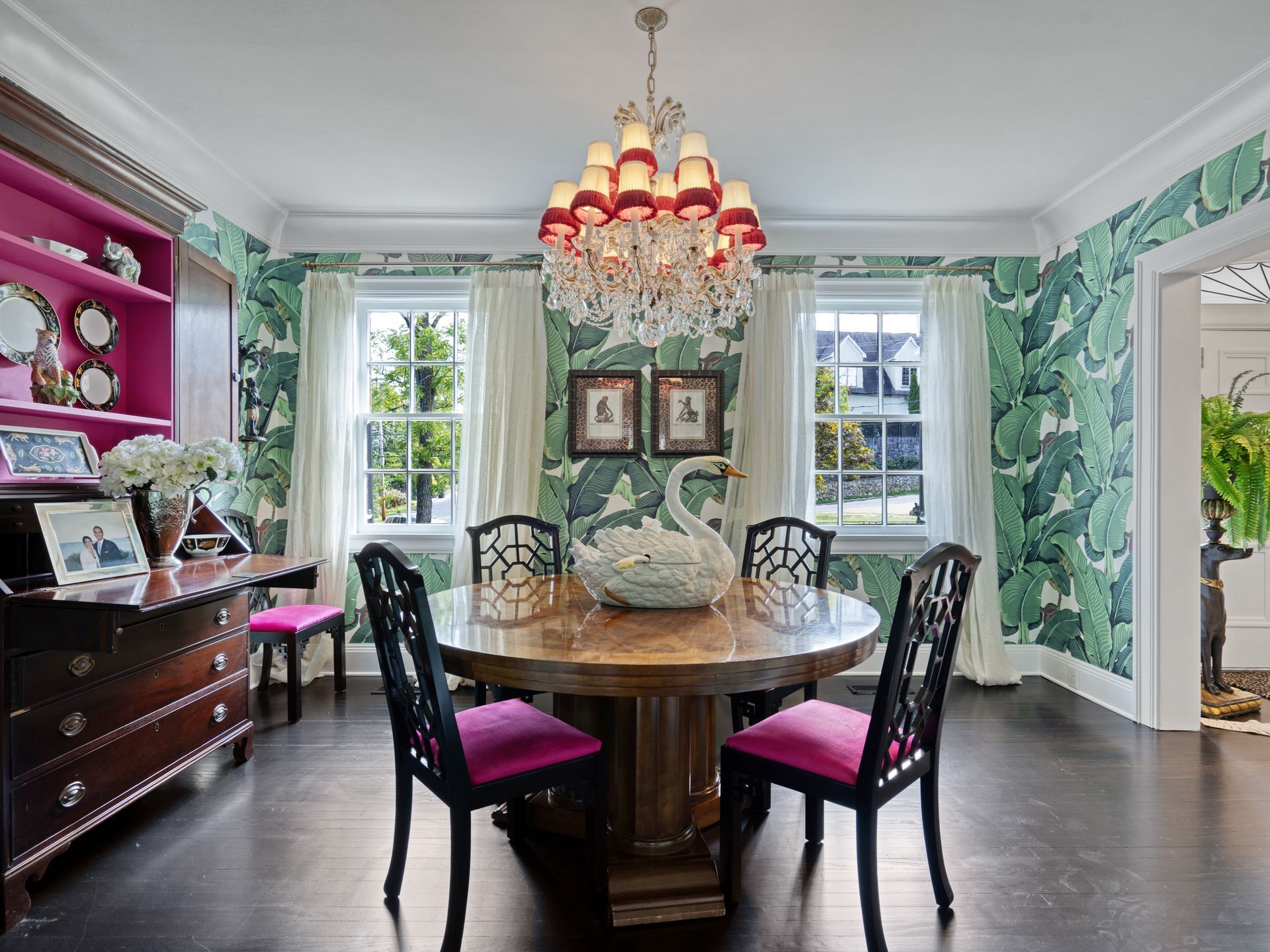 Elegant dining room with green leaf wallpaper, round table, pink chairs, and ornate chandelier.