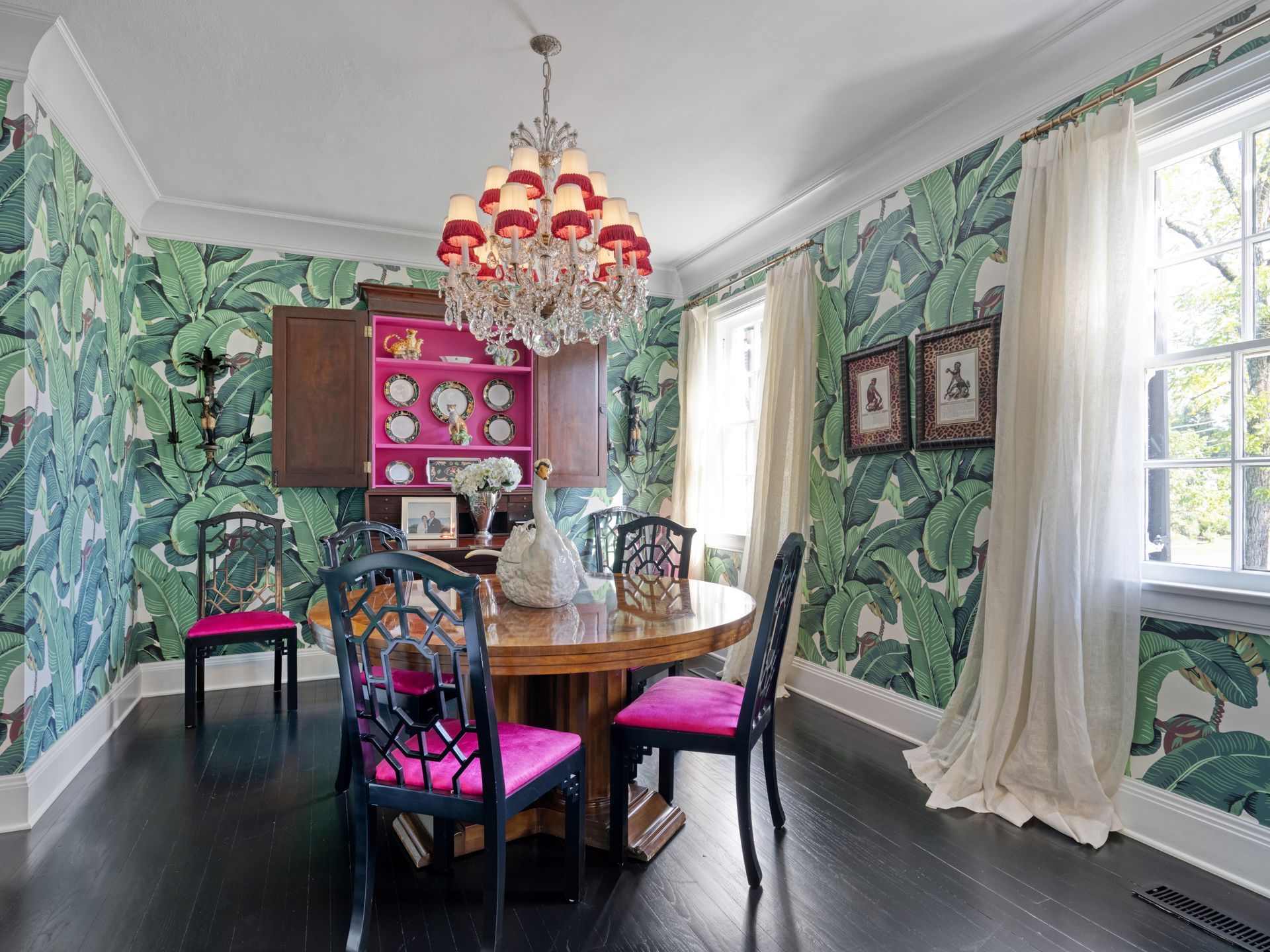 Dining room with green tropical wallpaper, a round table, and a red chandelier.