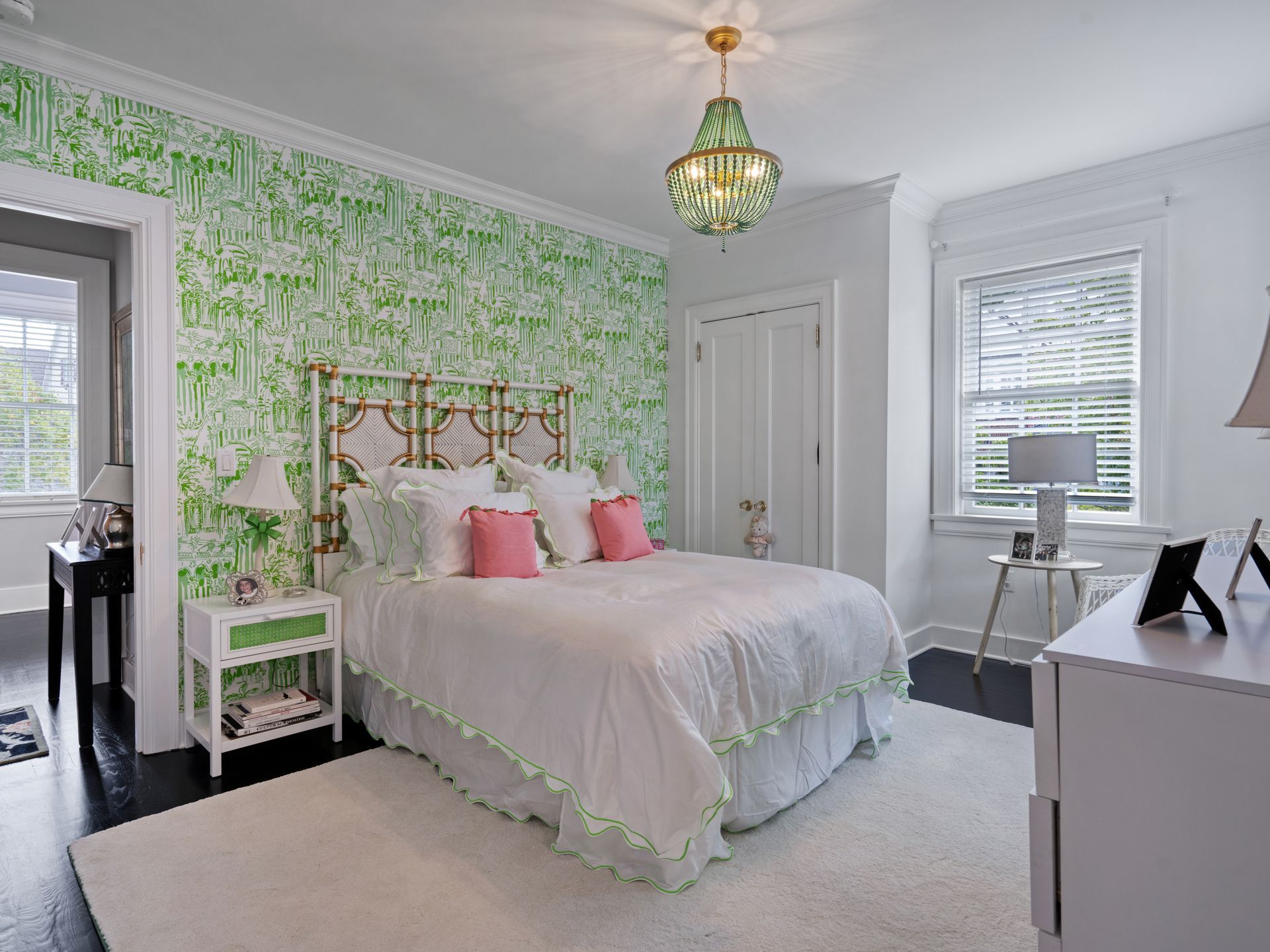 Bedroom with white and green patterned wallpaper, white bedding, gold headboard, and a green chandelier.