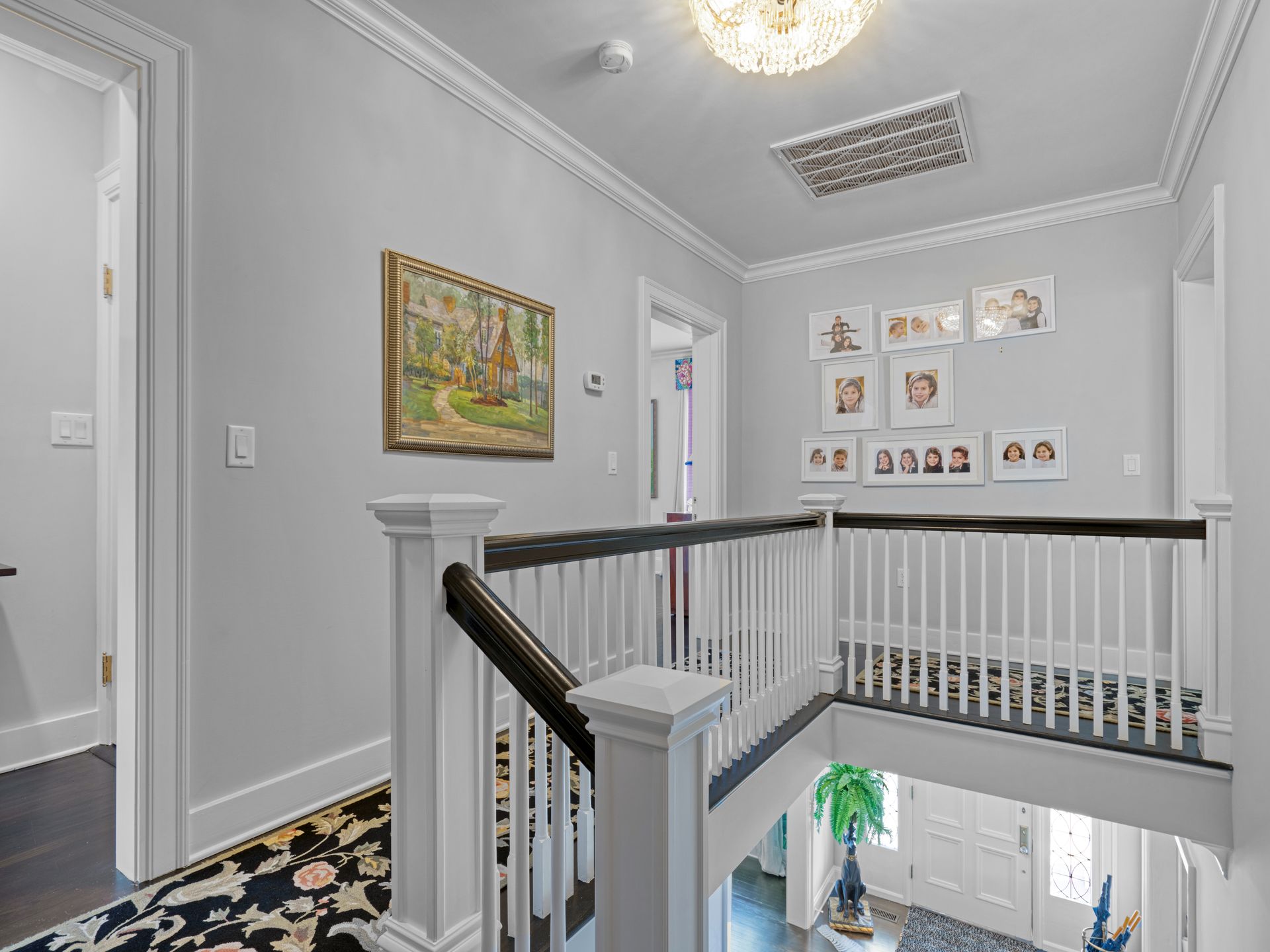 Hallway with white railing, artwork, and framed photos; light gray walls, dark wood floors.