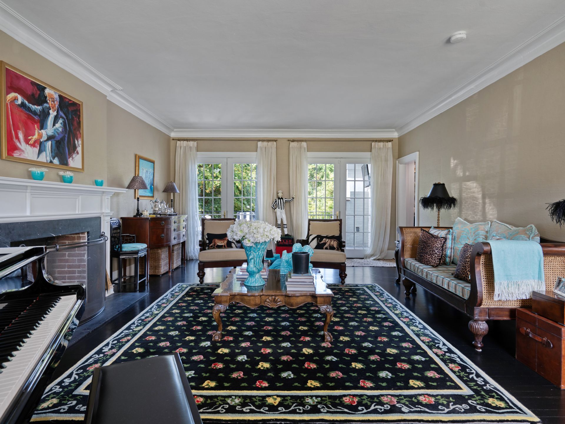 Living room with black piano, antique furniture, floral rug, and two doors leading outside.