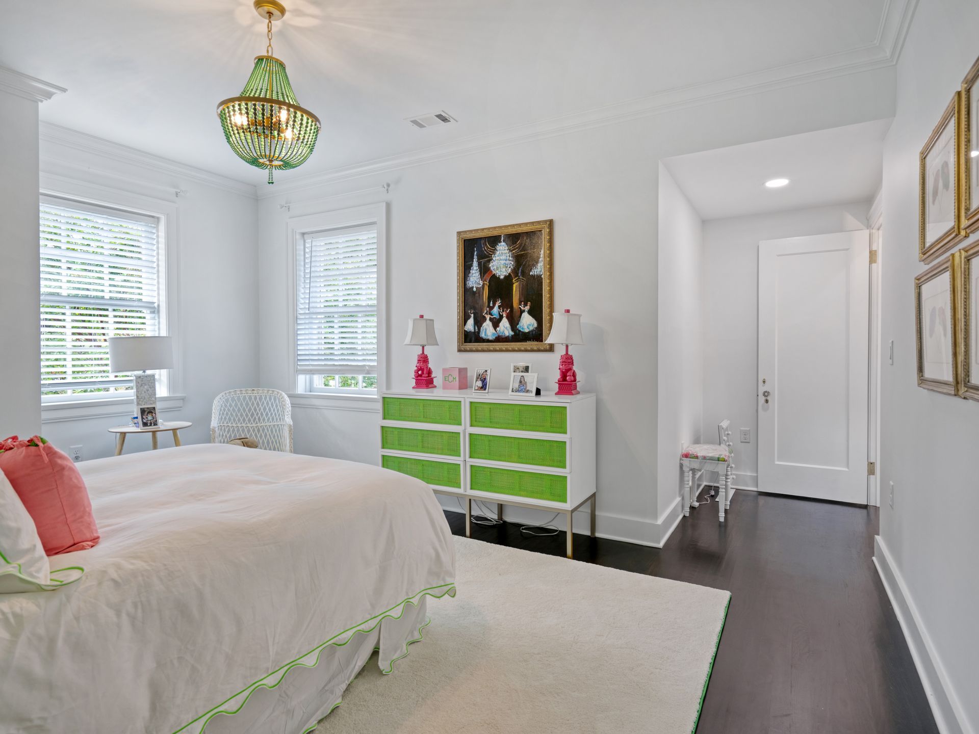 Bedroom with white walls, a green chandelier, and a white bed. A green and white dresser sits below a painting.