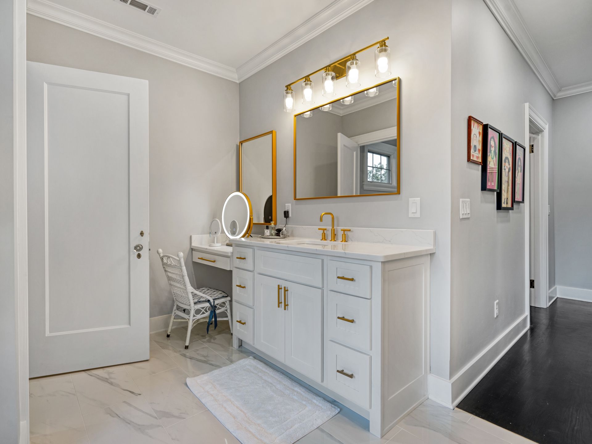 Bathroom with white vanity, gold accents, mirror, and a small dressing table.