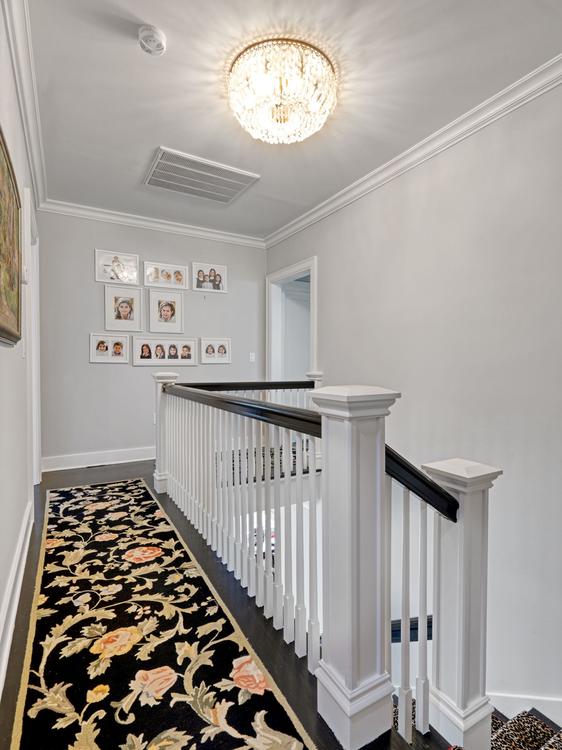Hallway with floral runner rug, white railing, and framed photos on the wall.