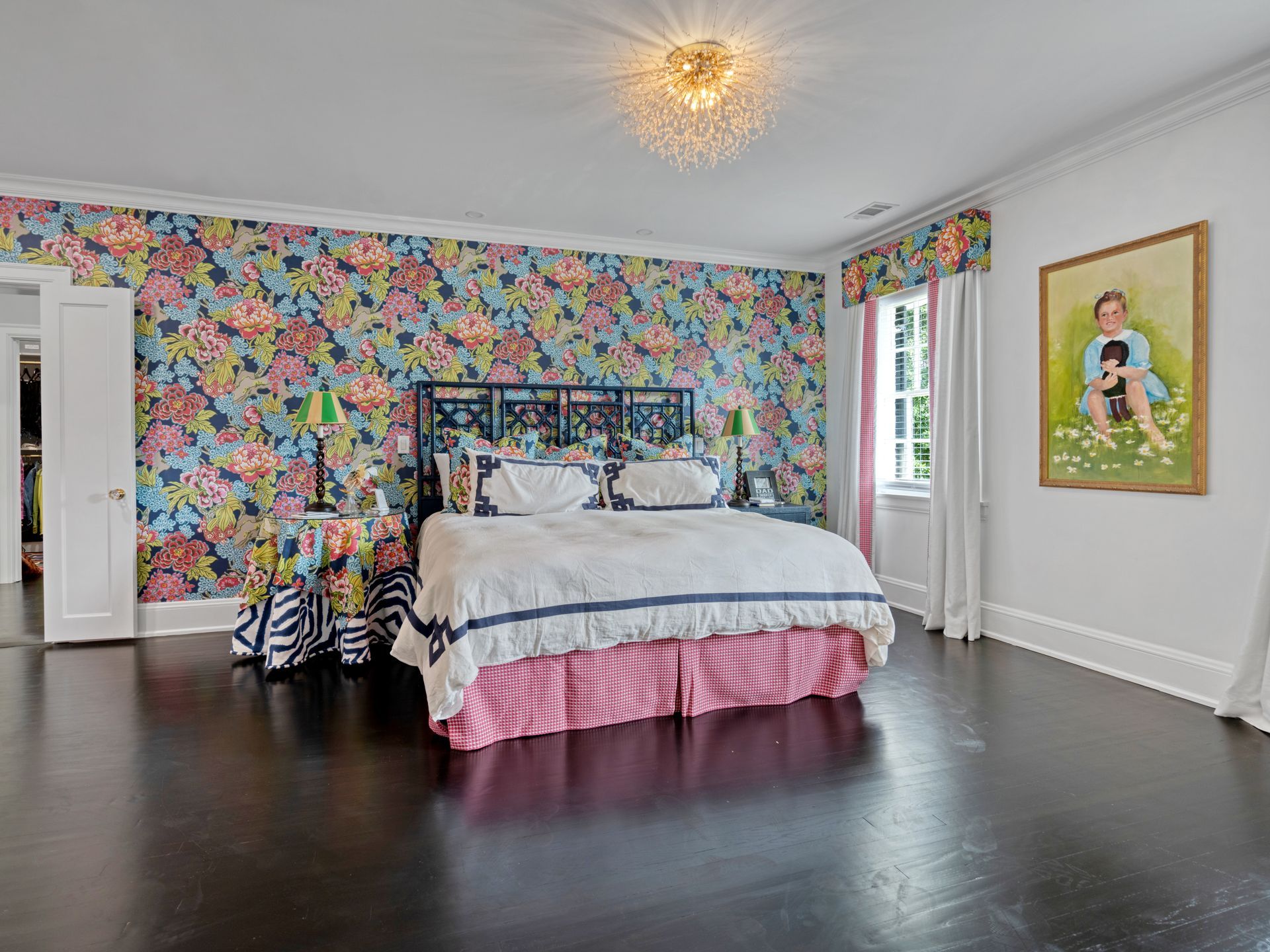 Bedroom with floral wallpaper, dark wood floors, bed, patterned nightstands, artwork, and crystal chandelier.