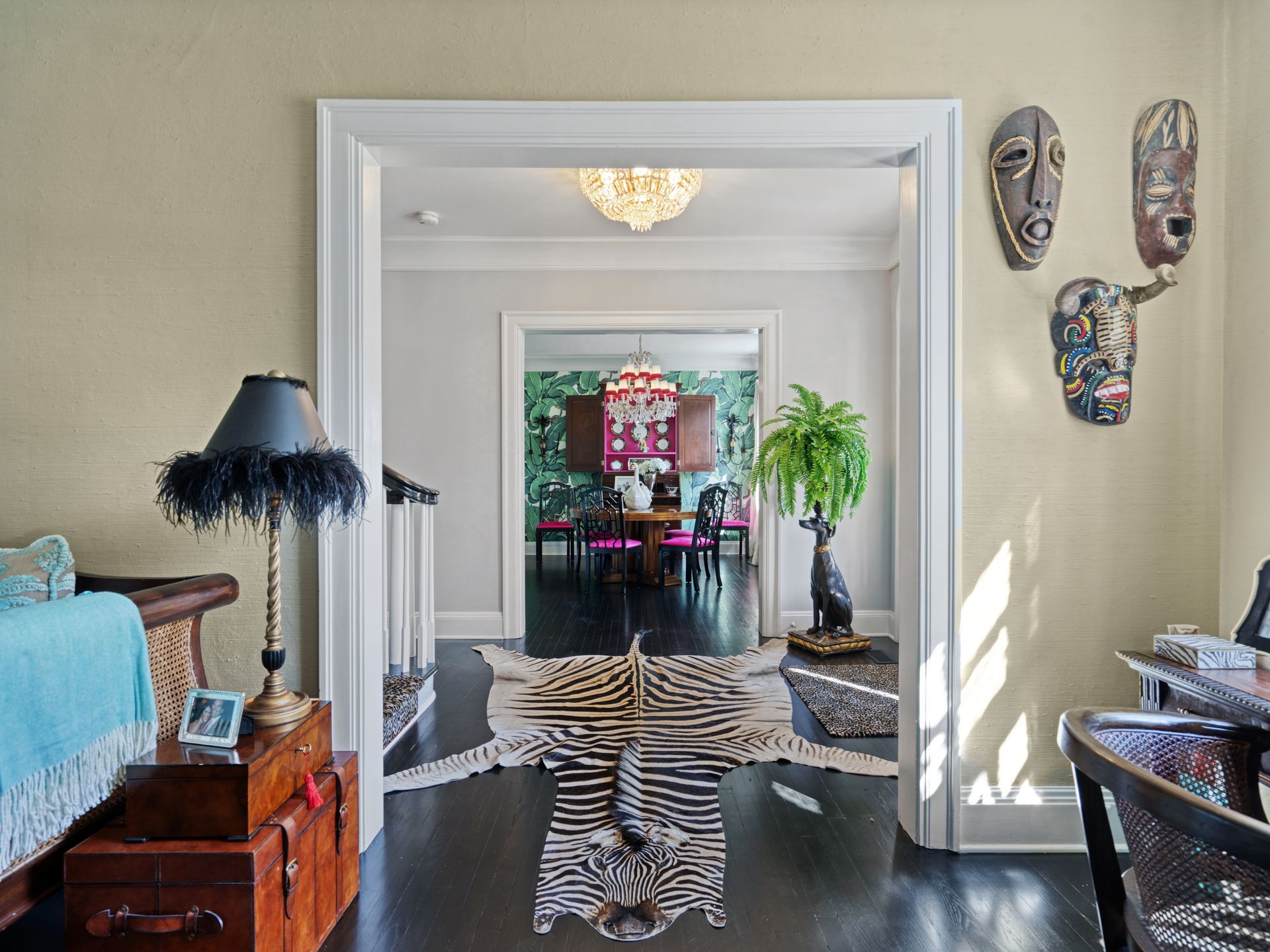 Entryway with zebra rug, dark wood floors, African masks, and a view into a dining room.