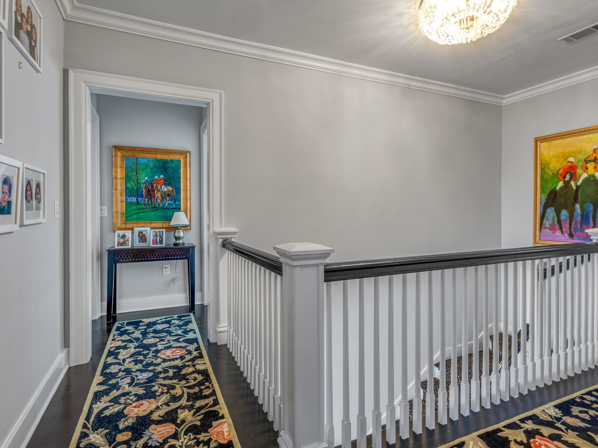 Hallway with gray walls, white trim, and a dark runner rug. Artwork and a railing are also visible.