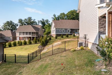 Houses with a black fence on a grassy hill, trees in the background, sunny day.