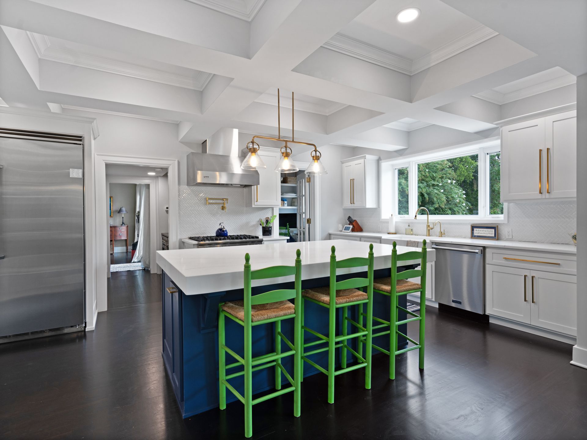 Spacious kitchen with blue island, green bar stools, white cabinets, and stainless steel appliances.