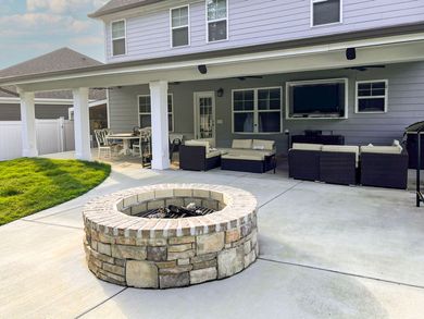 A backyard patio with a stone fire pit, seating, and a covered porch.