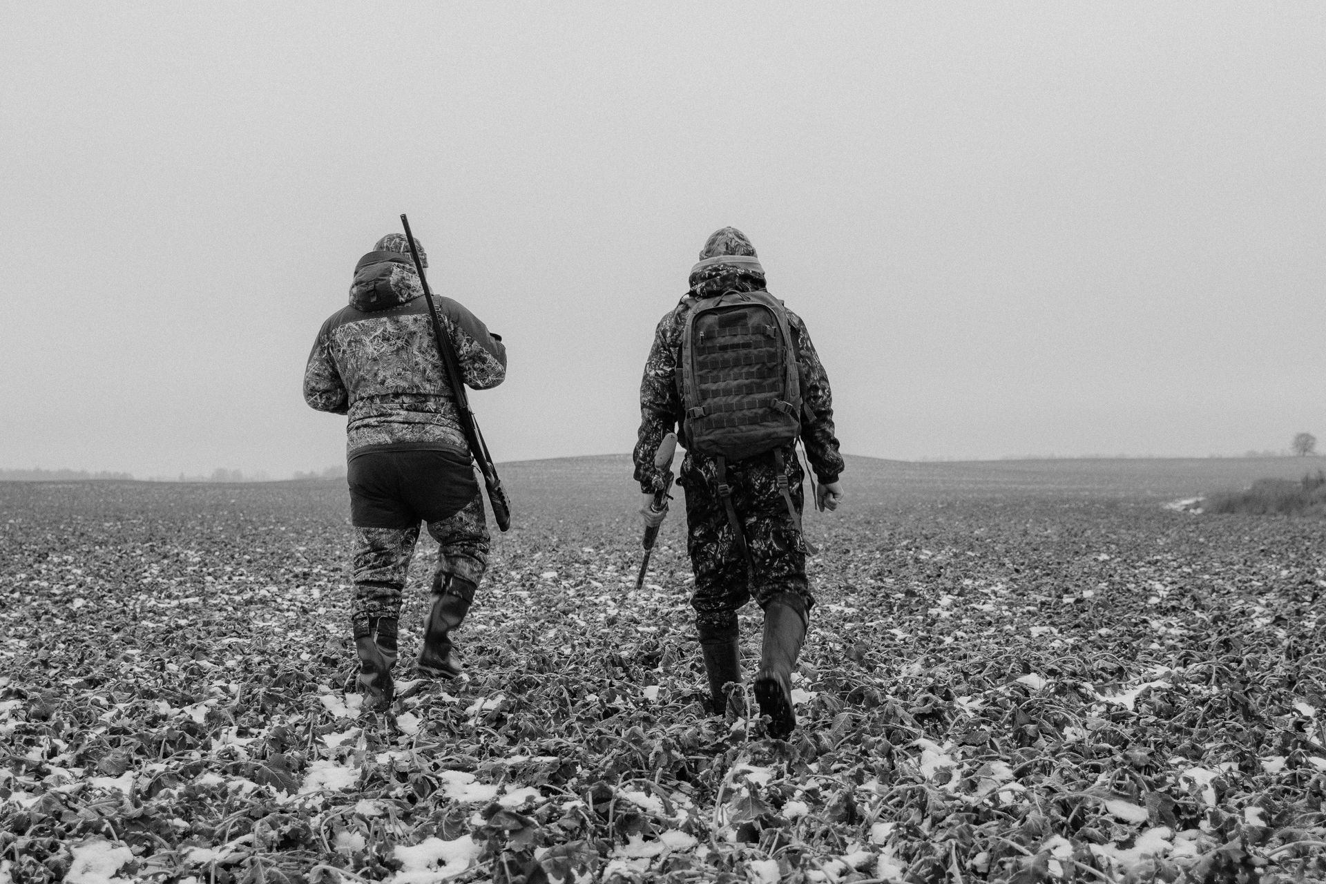 Two hunters are walking through a snowy field.