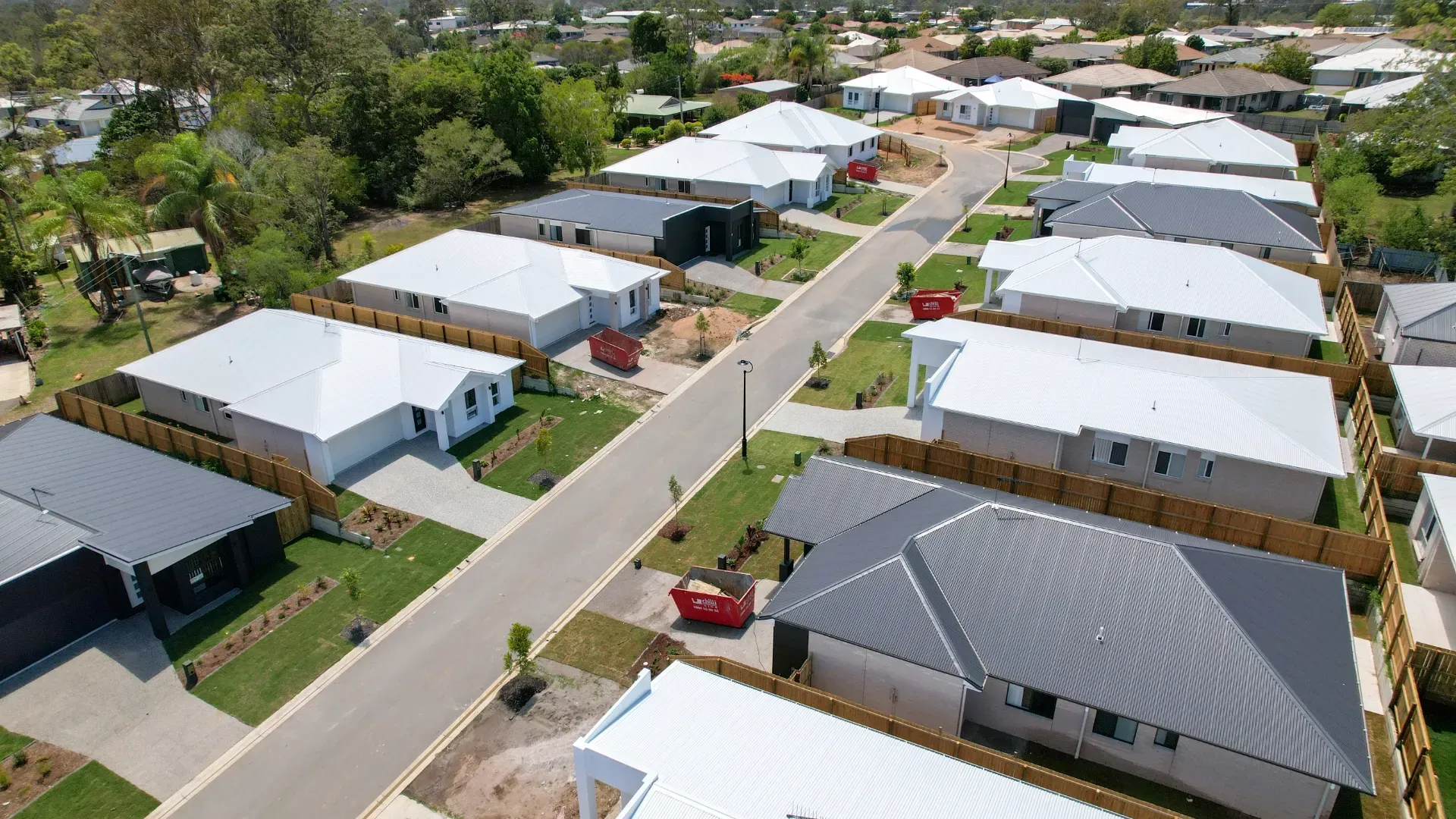 An aerial view of a suburban street featuring several rows of newly built, single-story houses with light and dark roofs.