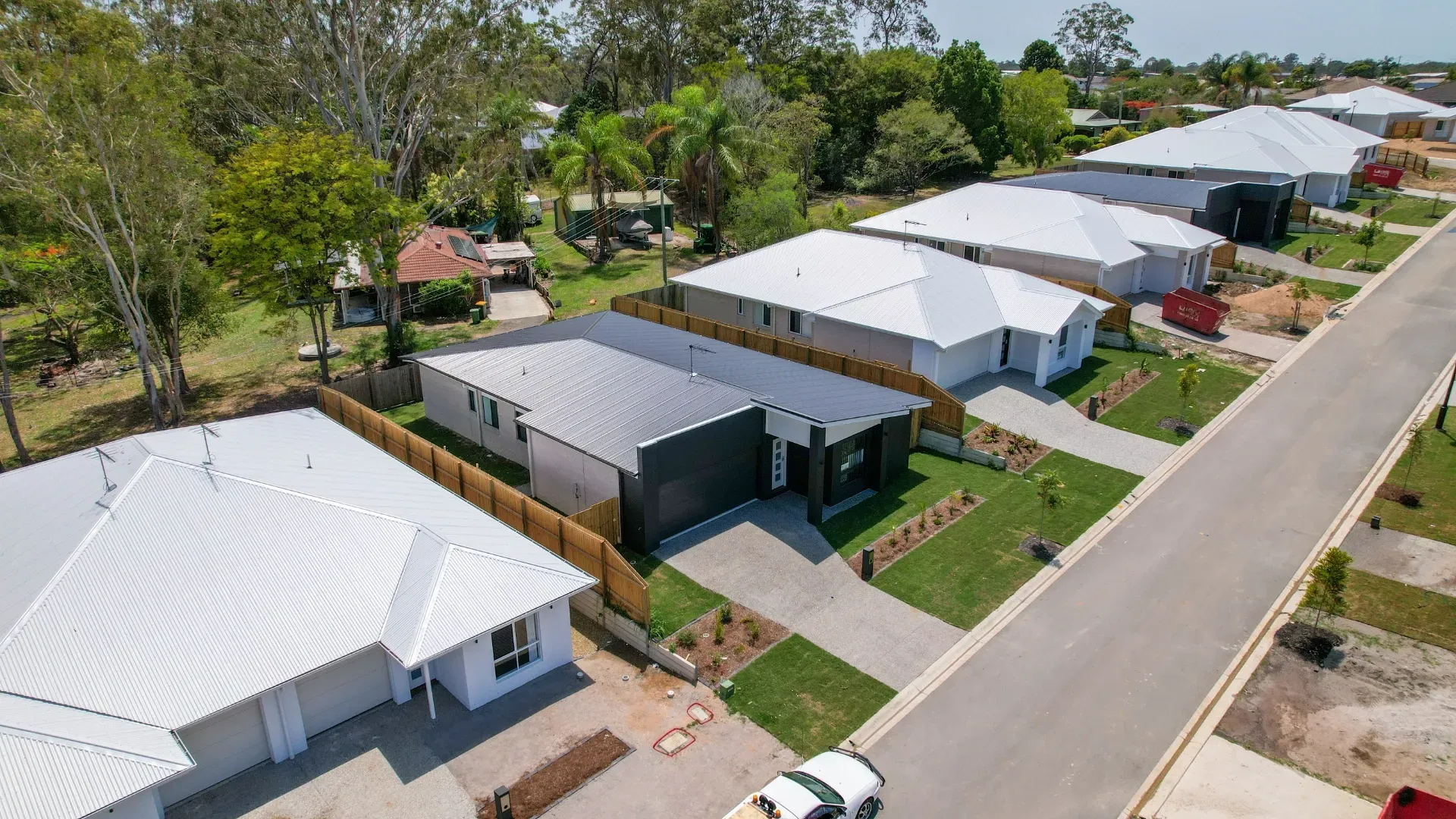 Aerial view of a suburban street featuring several modern, single-story houses with white roofs and front driveways.