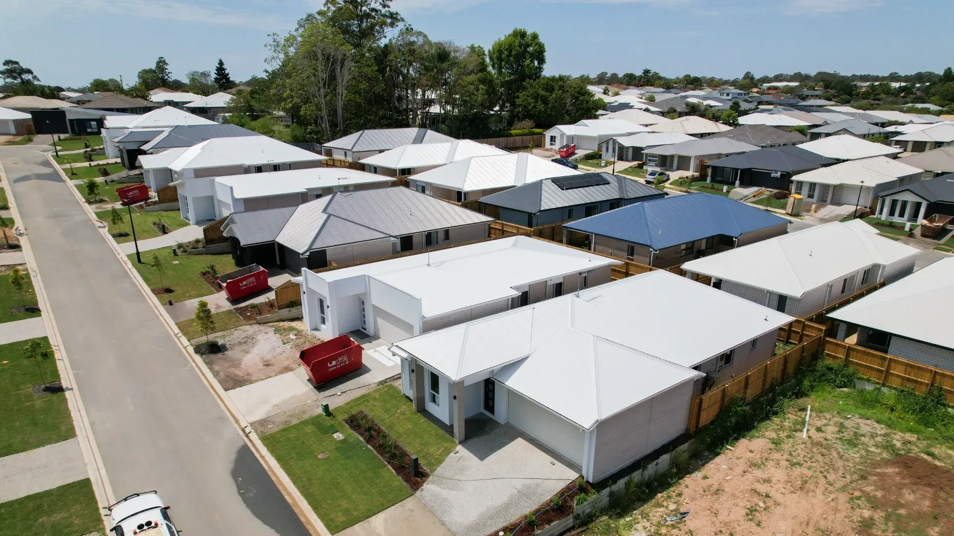 Aerial view of a residential neighborhood featuring rows of modern single-story houses with light-colored roofs.