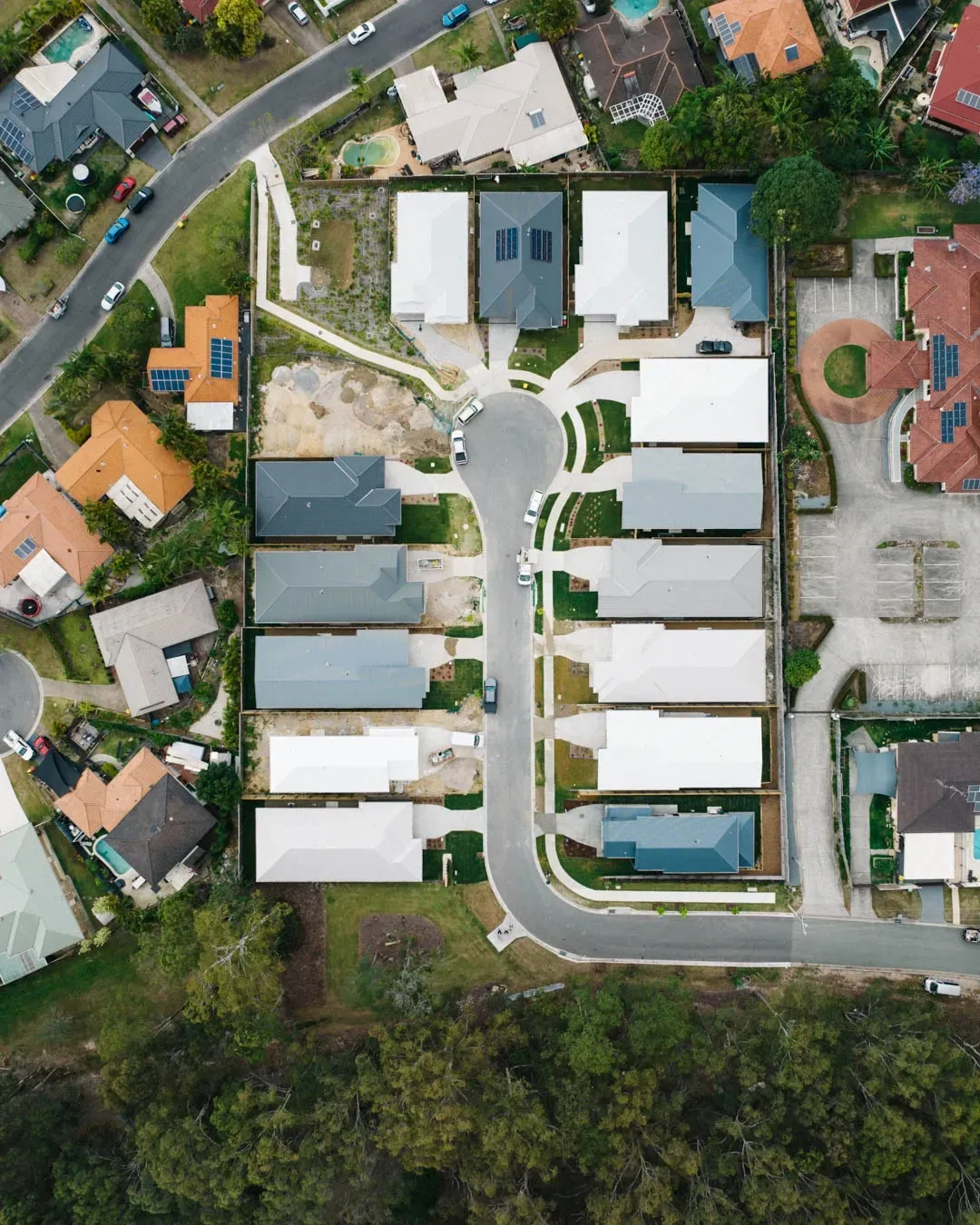 An aerial view of a suburban cul-de-sac featuring several modern, light-roofed homes surrounded by trees and roads.