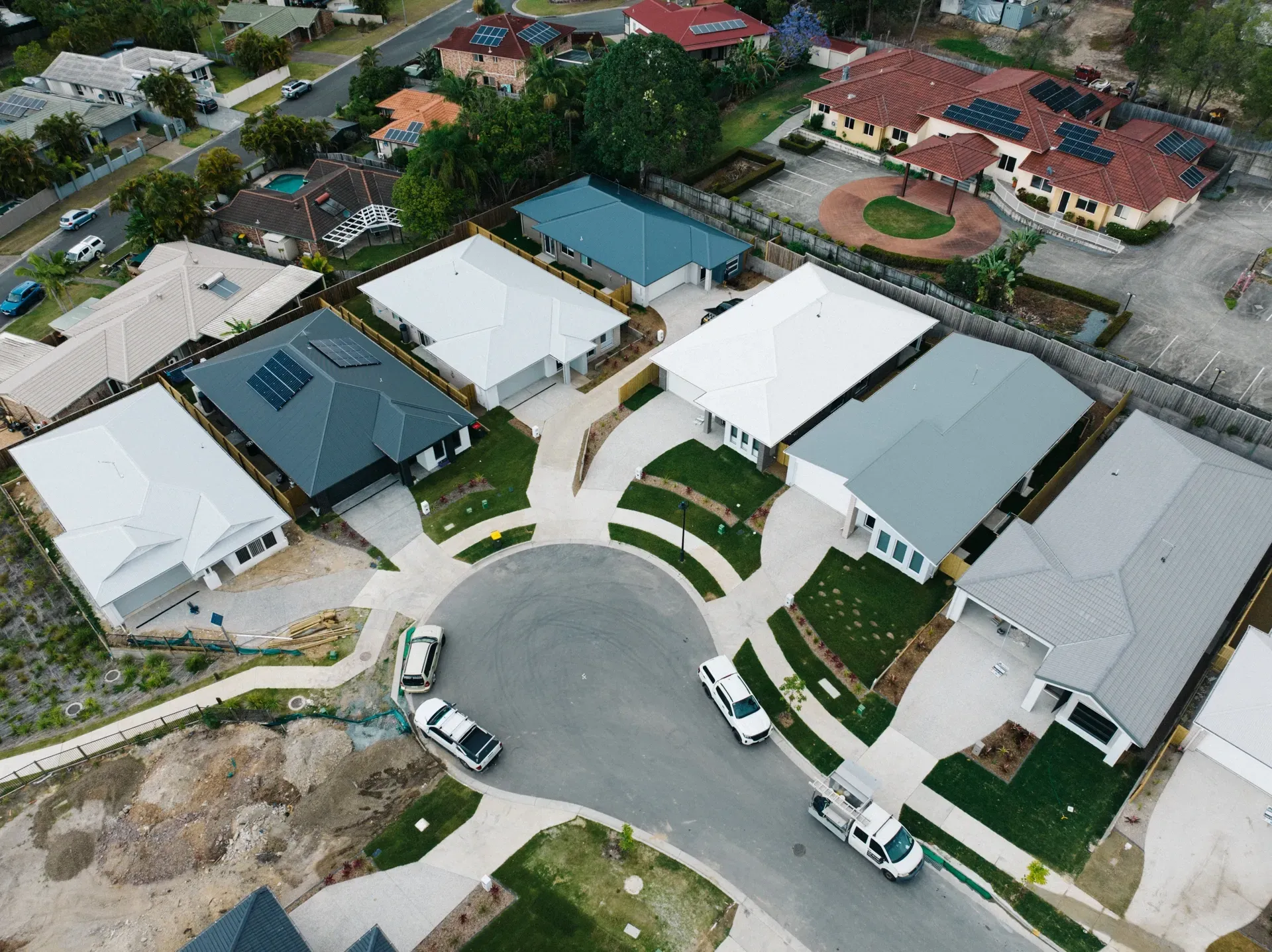 An aerial view of a suburban cul-de-sac with several modern houses and parked vehicles along the street.