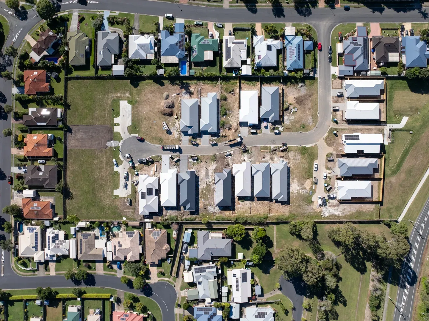 An aerial view of a suburban neighborhood showing single-family homes with gray roofs and surrounding grass lots.
