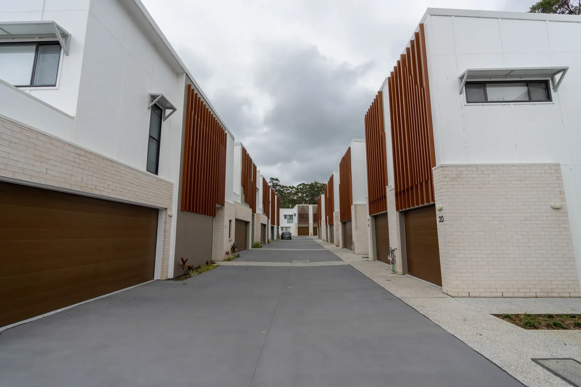 Row of modern white townhouses with brown garage doors and decorative wooden panels. — Smart Metal Roofing in Coomera, QLD