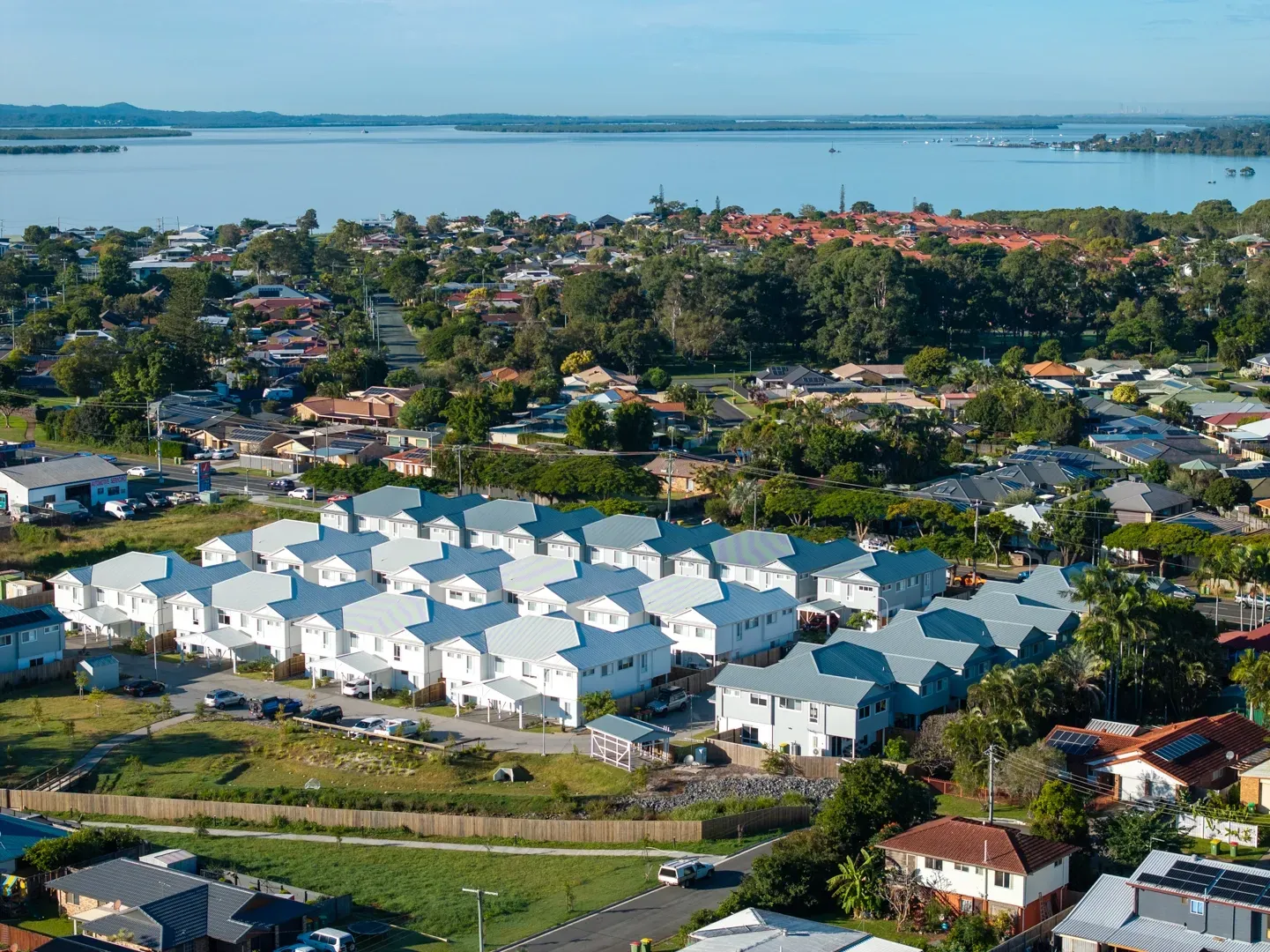 Aerial view of a suburban neighborhood with rows of houses and a lake in the background. — Smart Metal Roofing in Coomera, QLD