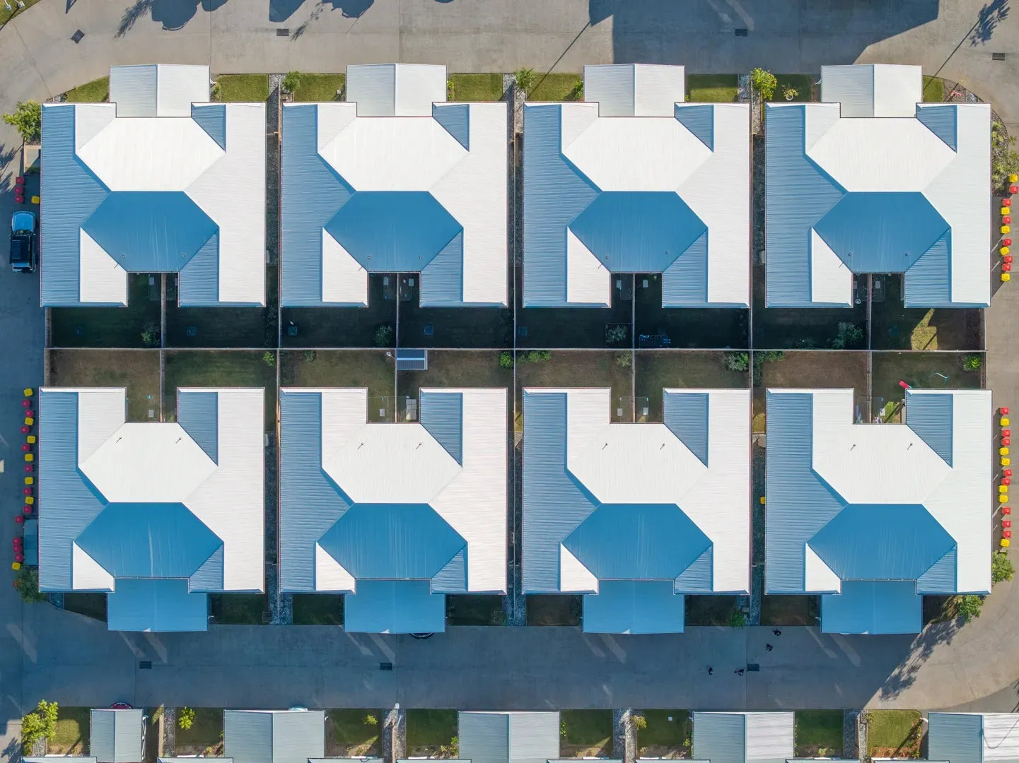 Aerial view of eight houses with white roofs and blue accents, arranged in two rows with driveways. — Smart Metal Roofing in Coomera, QLD
