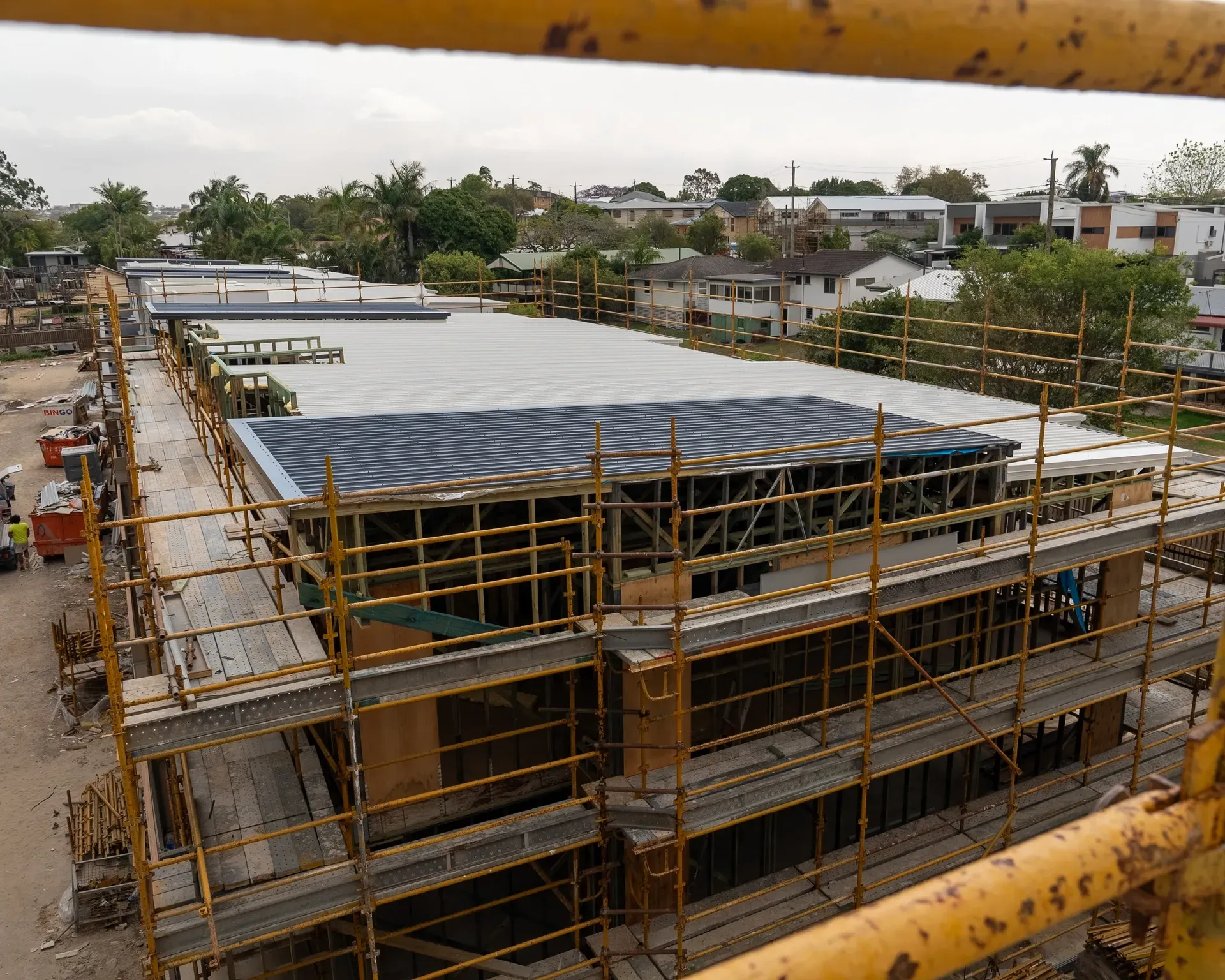 Construction site with scaffolding around a two-story building. The roof has dark blue and grey panels. — Smart Metal Roofing in Coomera, QLD