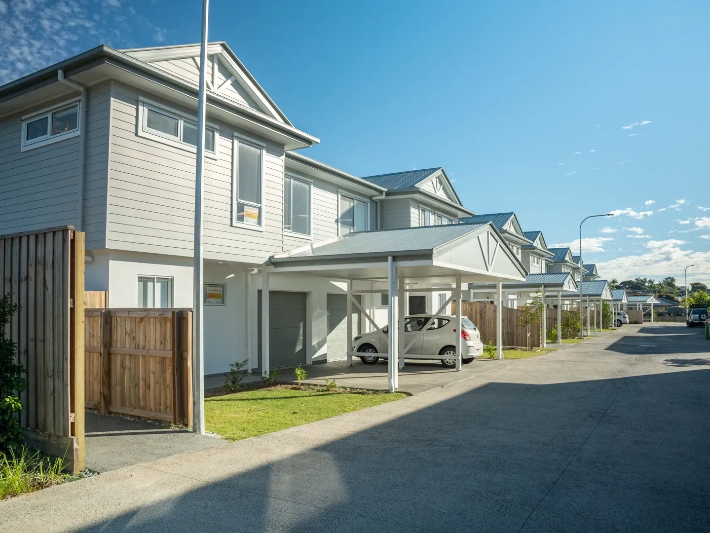 Row of gray townhouses with carports on a sunny street, a white car is parked. — Smart Metal Roofing in Coomera, QLD