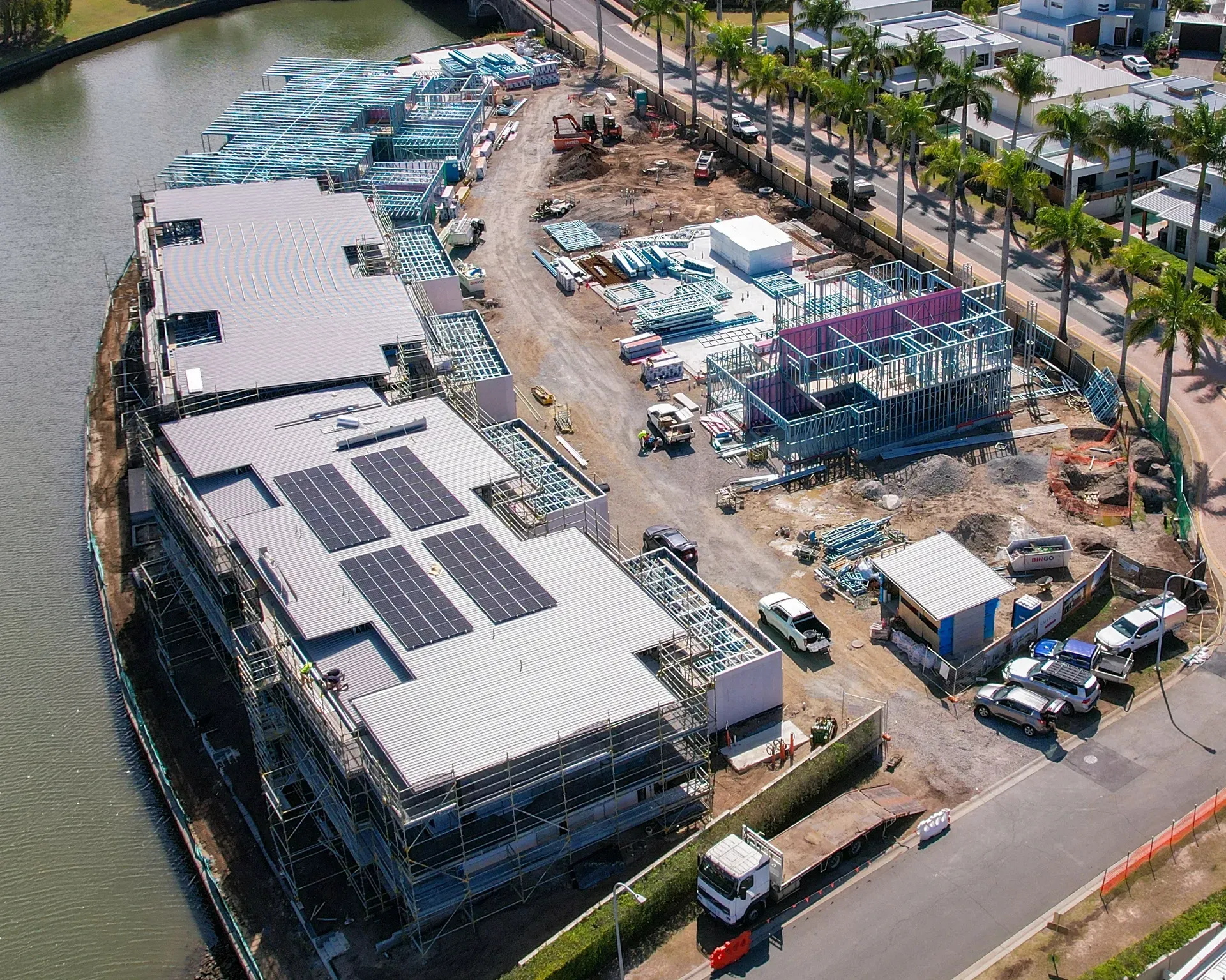Construction site with multi-story buildings, solar panels, and construction materials near water. — Smart Metal Roofing in Coomera, QLD