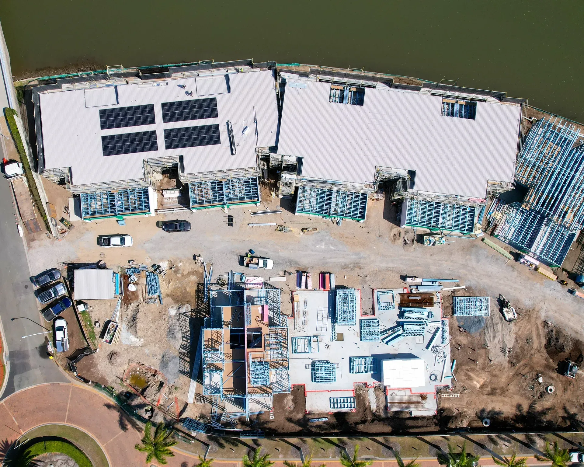 Aerial view of a construction site next to water, showing partially built buildings and materials. — Smart Metal Roofing in Coomera, QLD