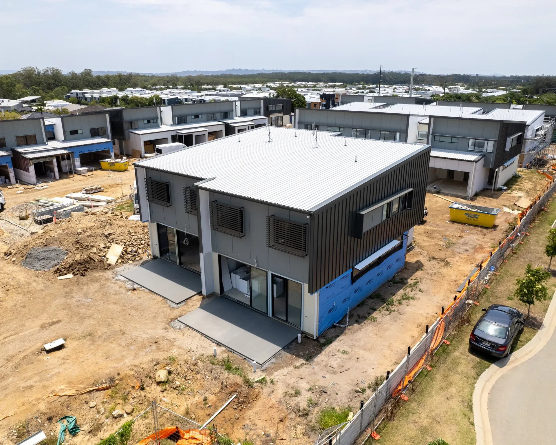 Aerial view of new construction: a two-story modern house with grey siding, corrugated roof, and surrounding dirt and construction materials. — Smart Metal Roofing in Coomera, QLD