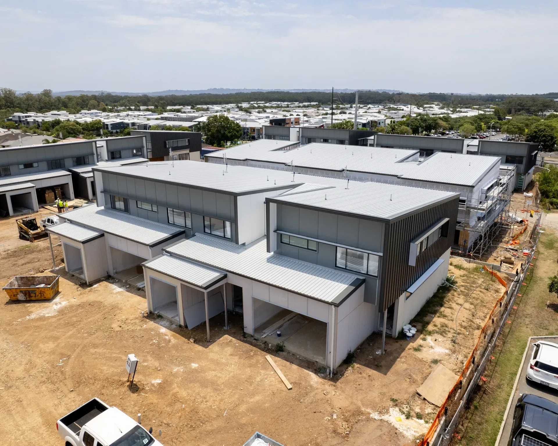 Construction of modern buildings with gray roofs and white walls, viewed from above, with a blue sky. — Smart Metal Roofing in Coomera, QLD