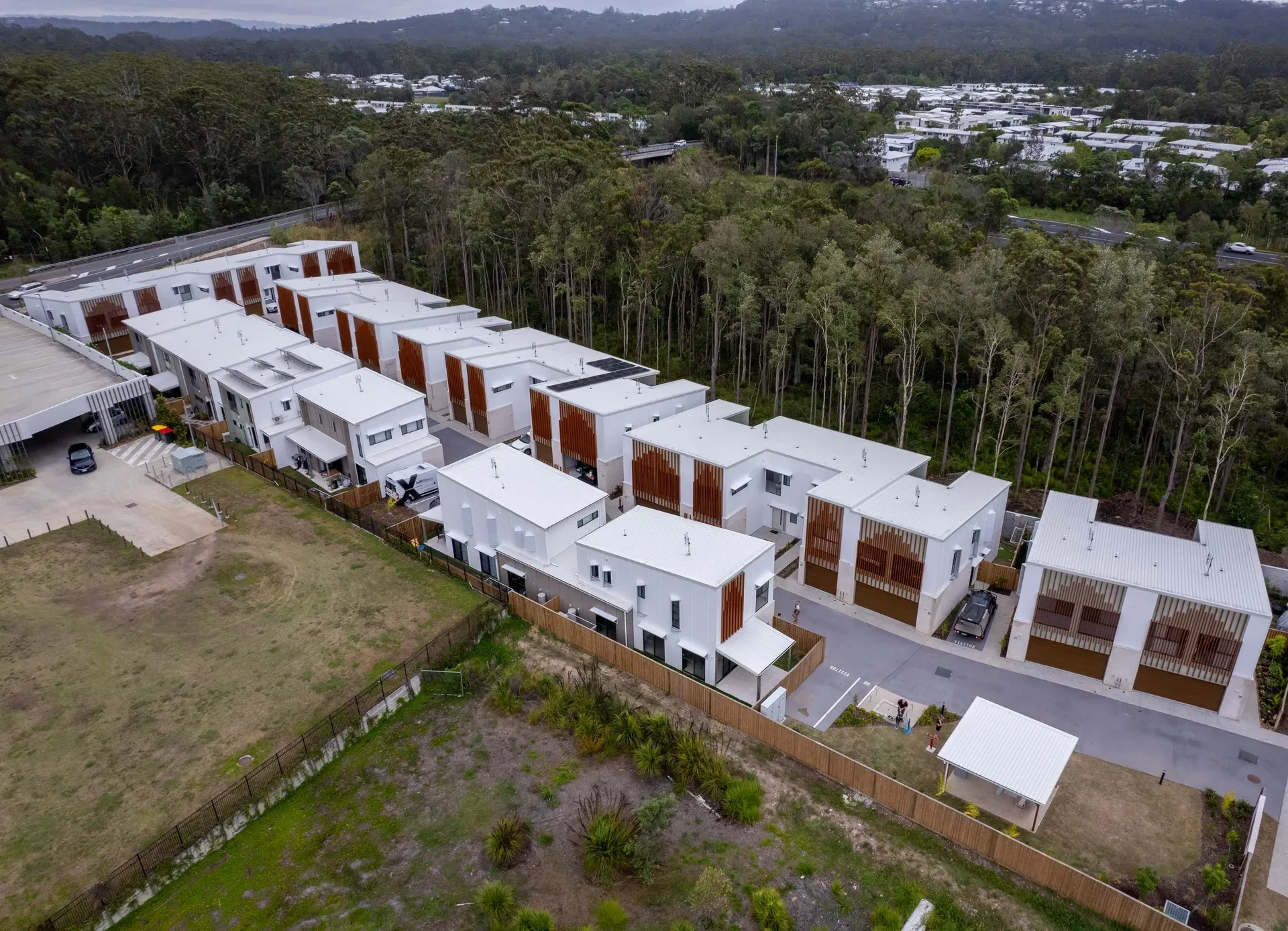 Aerial view of a row of modern townhouses with white walls and brown accents, set against a backdrop of trees. — Smart Metal Roofing in Coomera, QLD