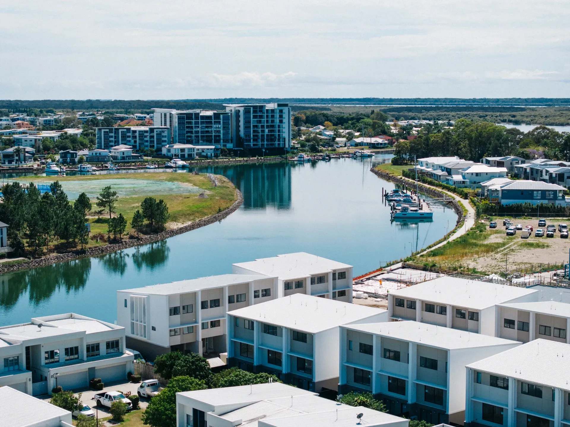 Waterfront cityscape with white buildings, a waterway, and clear skies. — Smart Metal Roofing in Coomera, QLD