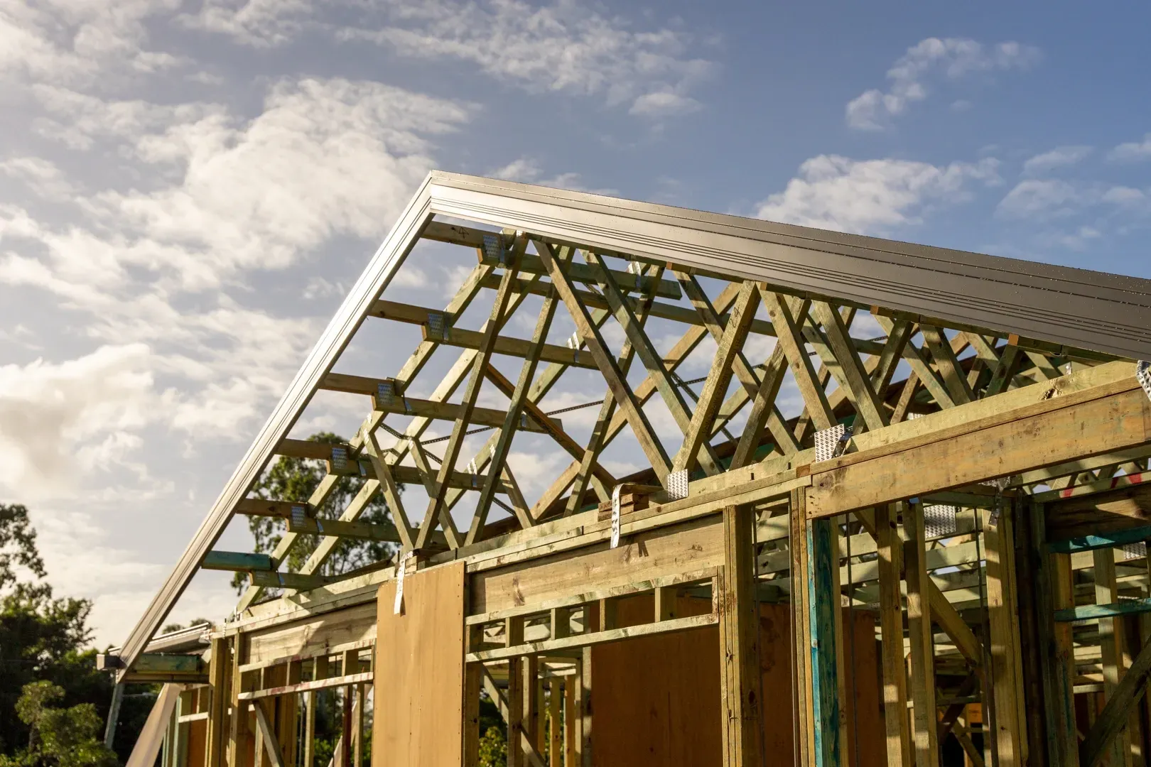 Wooden framework of a house under construction with a partly installed roof against a cloudy sky. — Smart Metal Roofing in Coomera, QLD