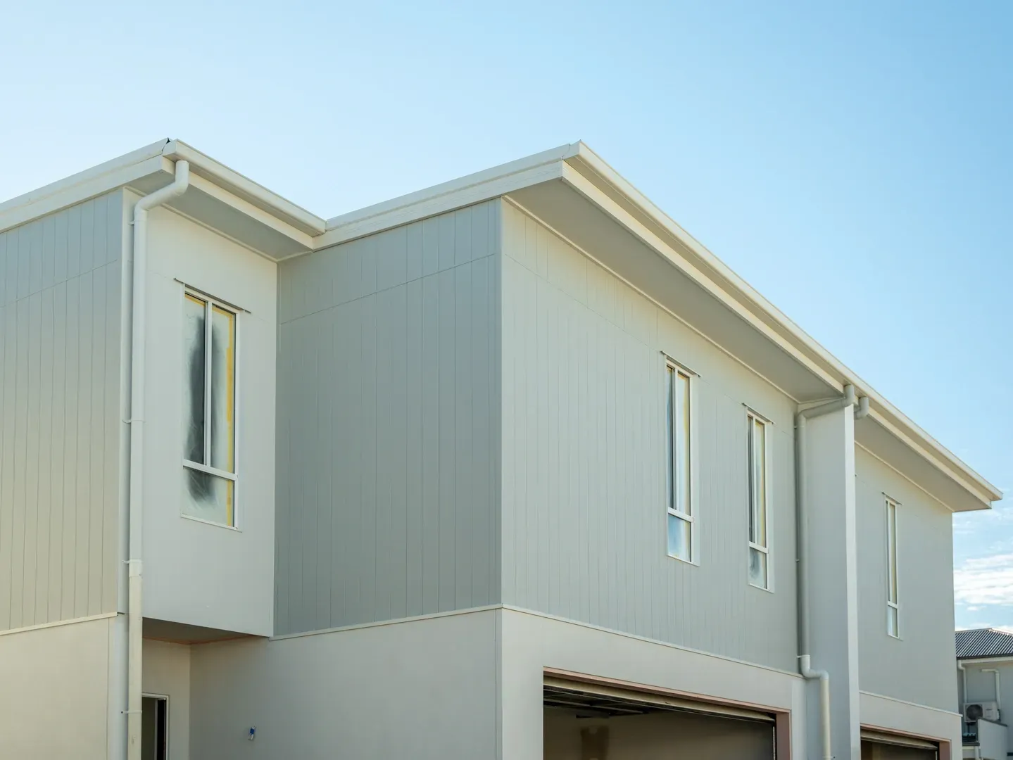 Modern multi-unit house with light gray panel siding, white trim, and a blue sky. — Smart Metal Roofing in Coomera, QLD