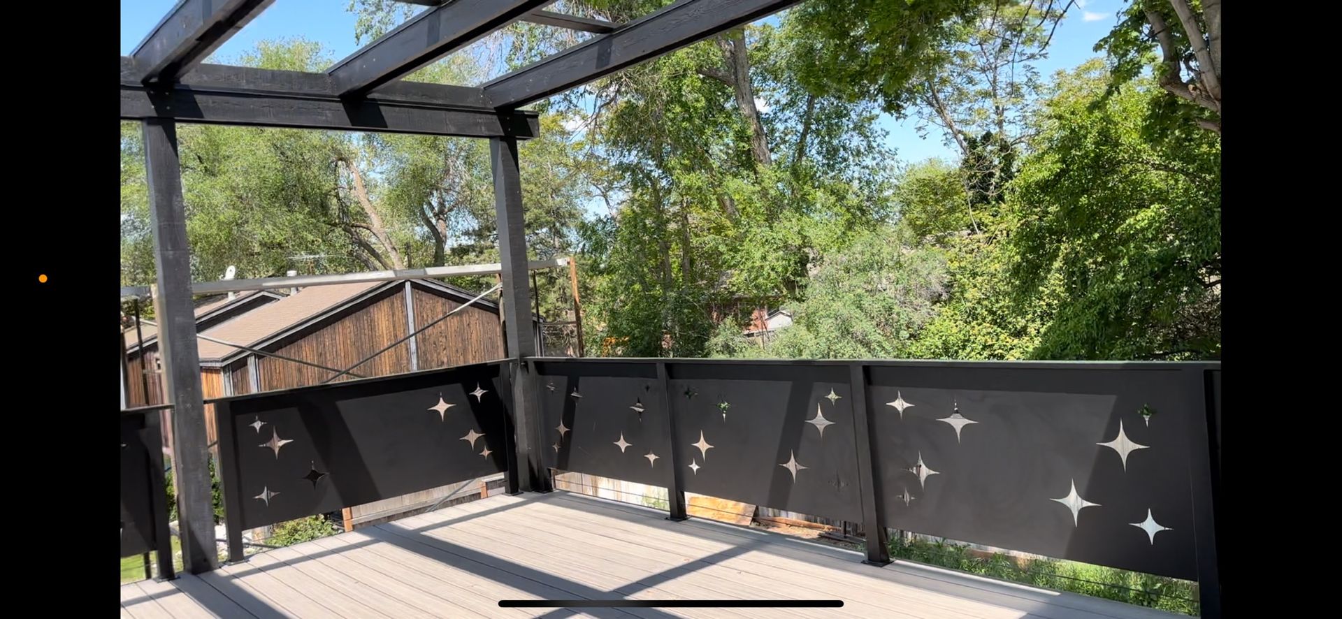 A balcony with a pergola and trees in the background.