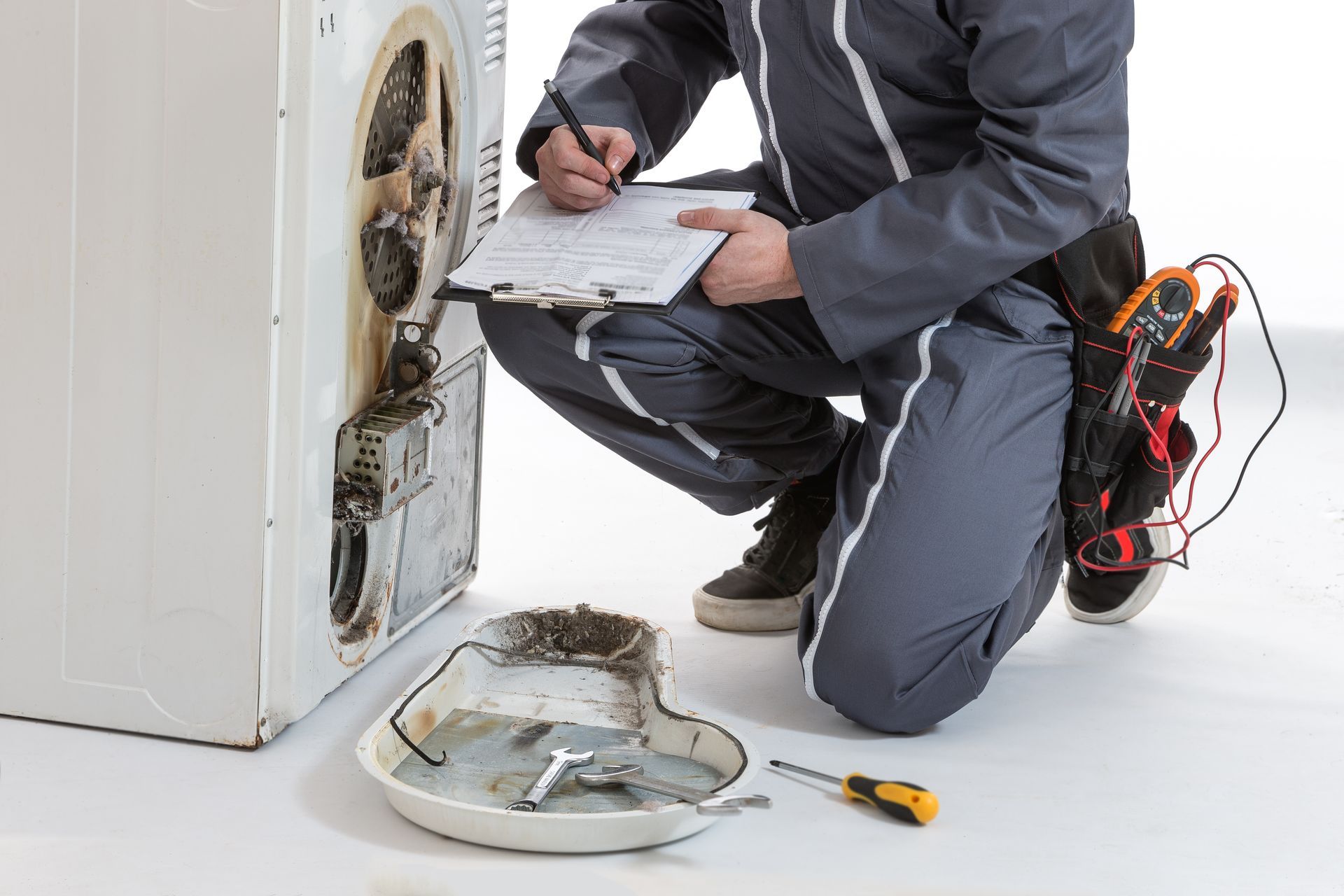 Technician inspecting and repairing a front-loading washer with tools on the floor