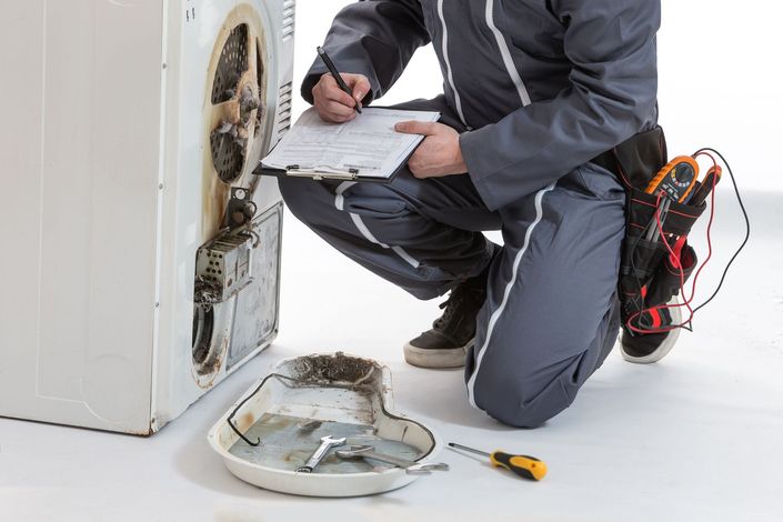 Technician inspecting and repairing a front-loading washer with tools on the floor