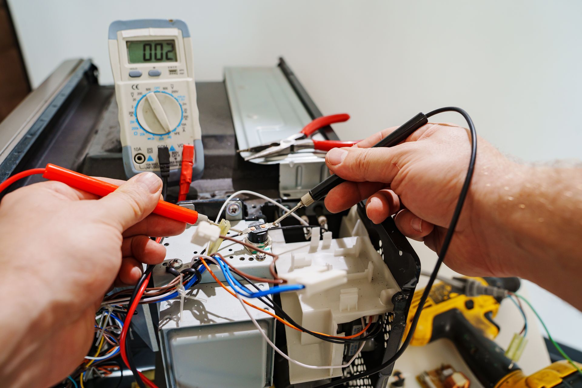 Hands testing an electronic circuit with a multimeter and red probes on a workbench