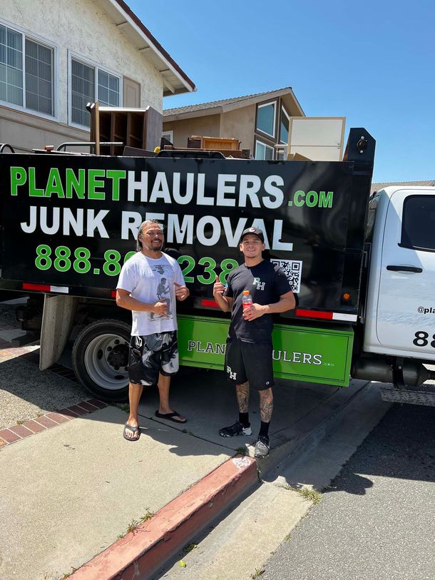 Two men are standing in front of a junk removal truck.