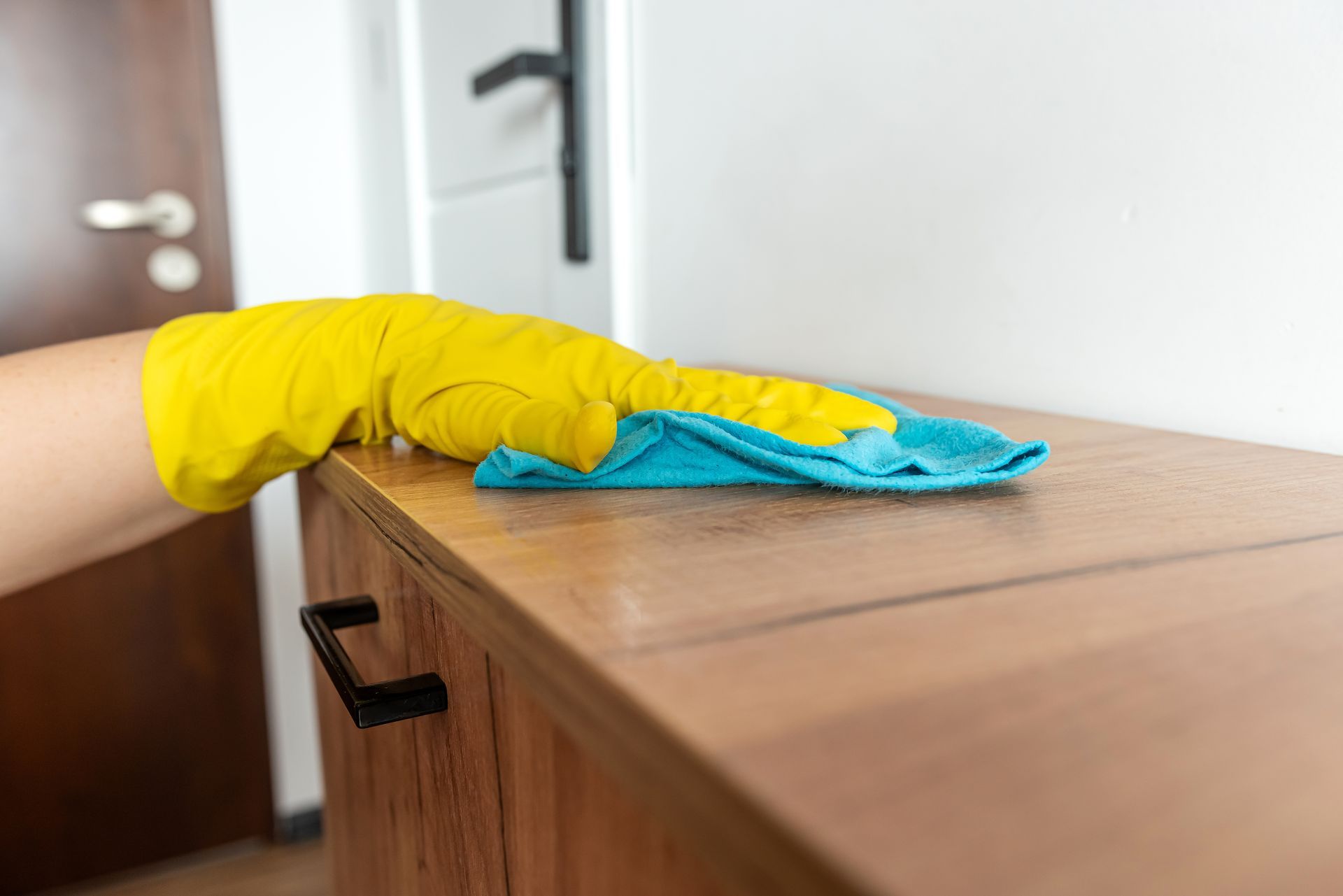 A person wearing yellow gloves is cleaning a wooden cabinet with a cloth.