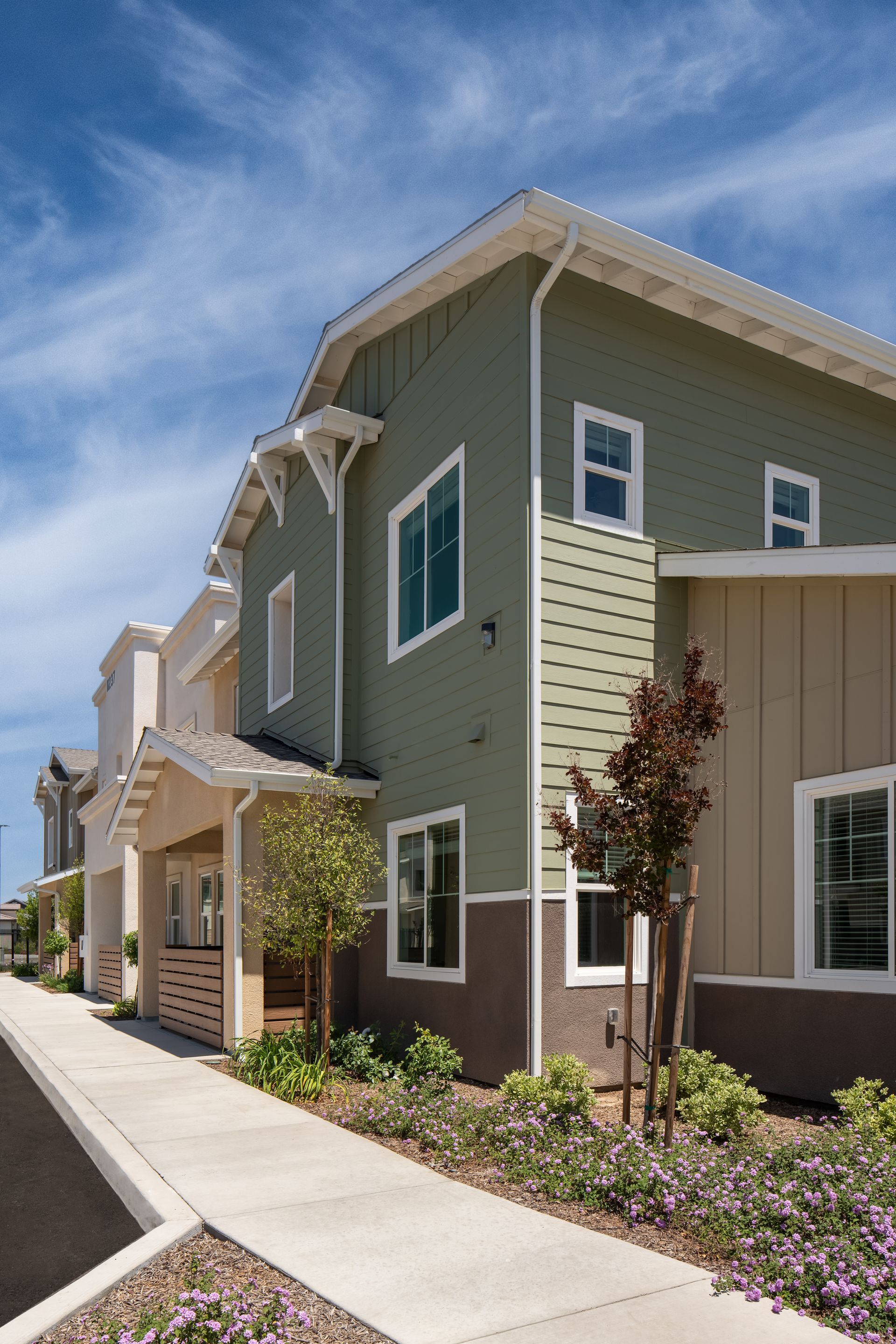 Townhouses with green and beige siding under a blue sky.