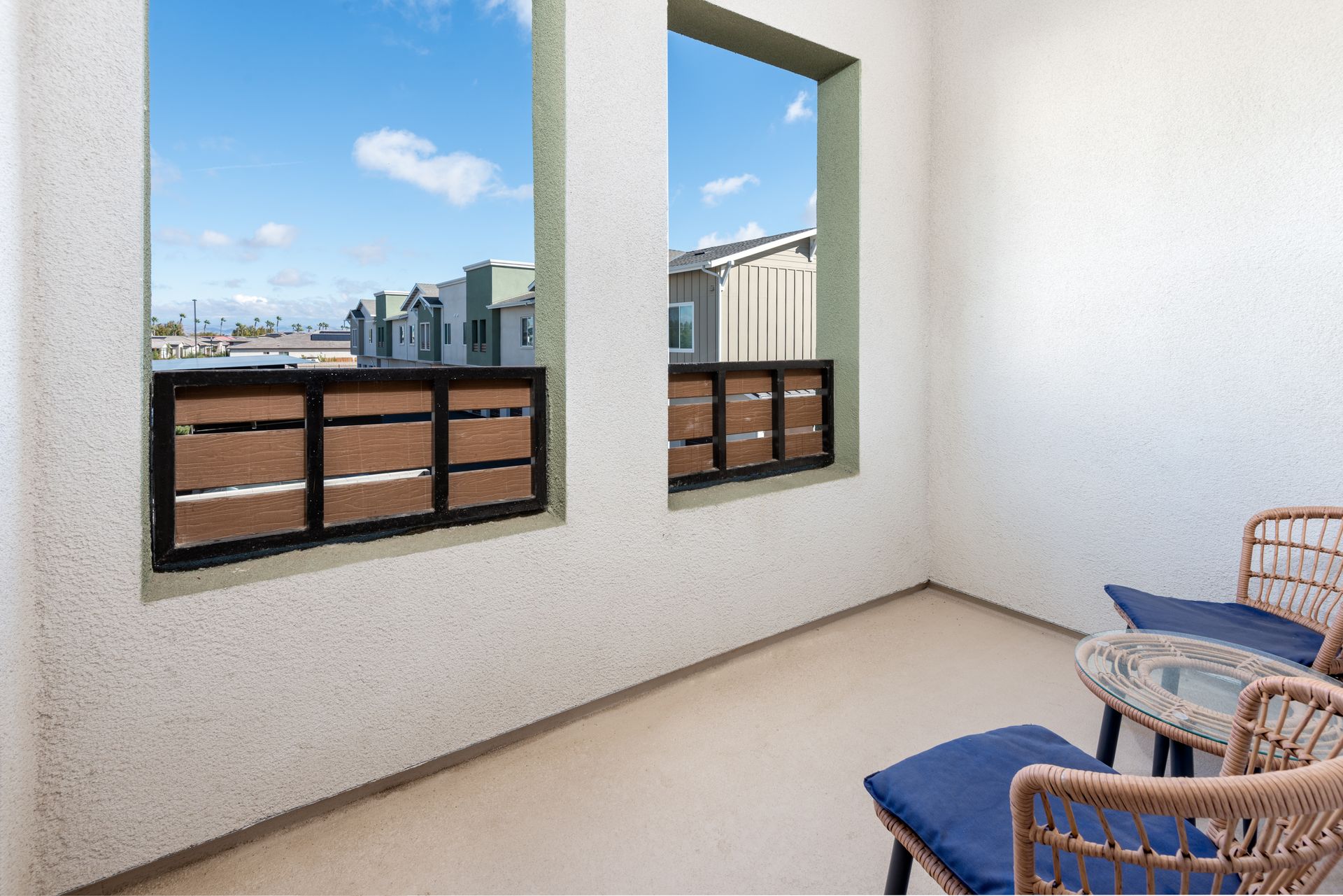 Balcony with two chairs, a small table, and windows overlooking a neighborhood.