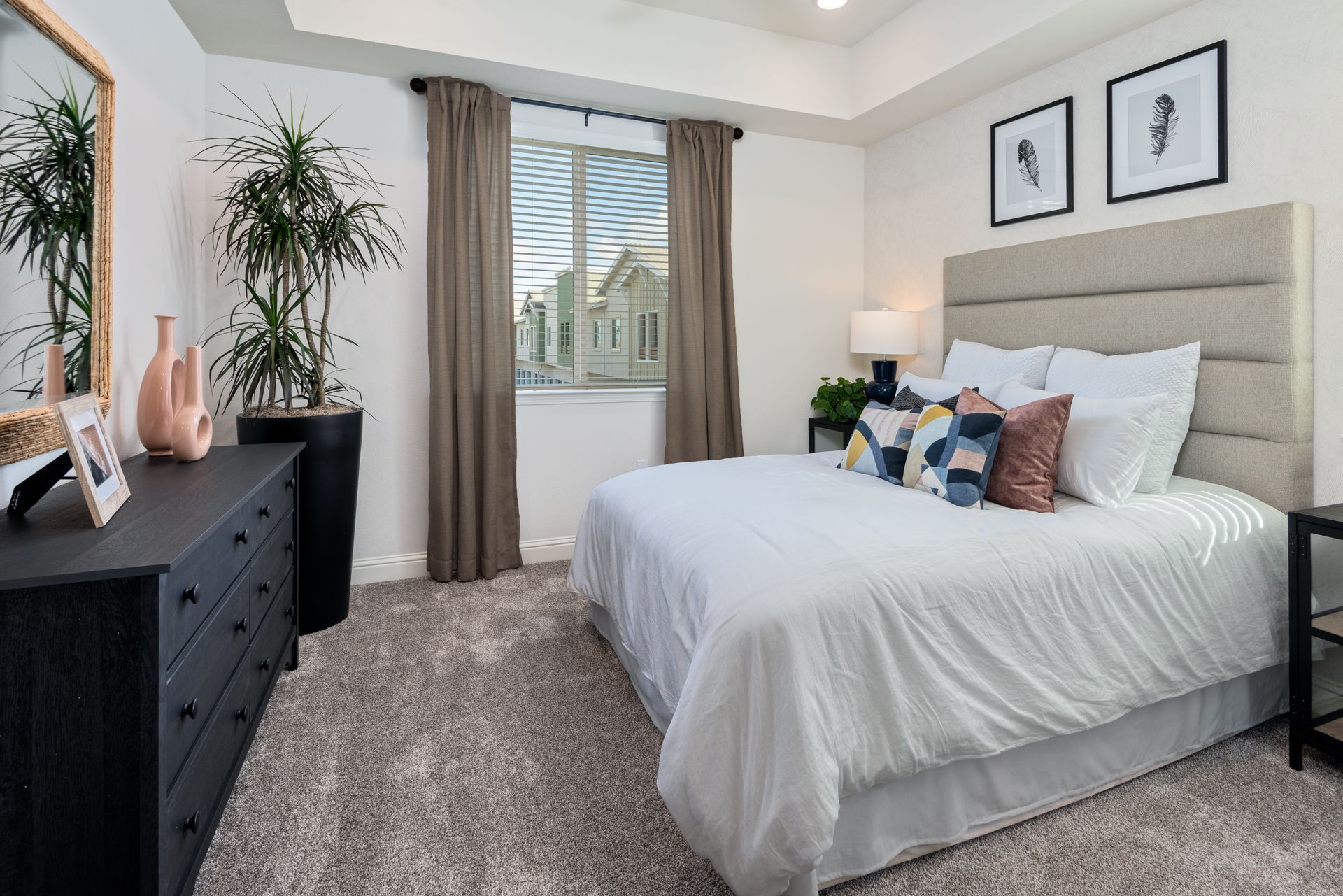 Bedroom with a white bed, dark dresser, neutral carpet, and large window with brown curtains.