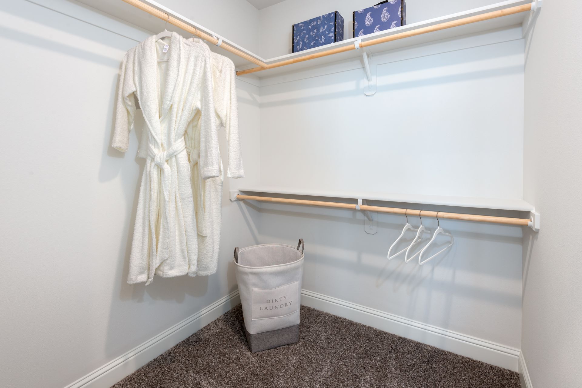 Small walk-in closet with white robes hanging, a laundry basket, and some shelves.